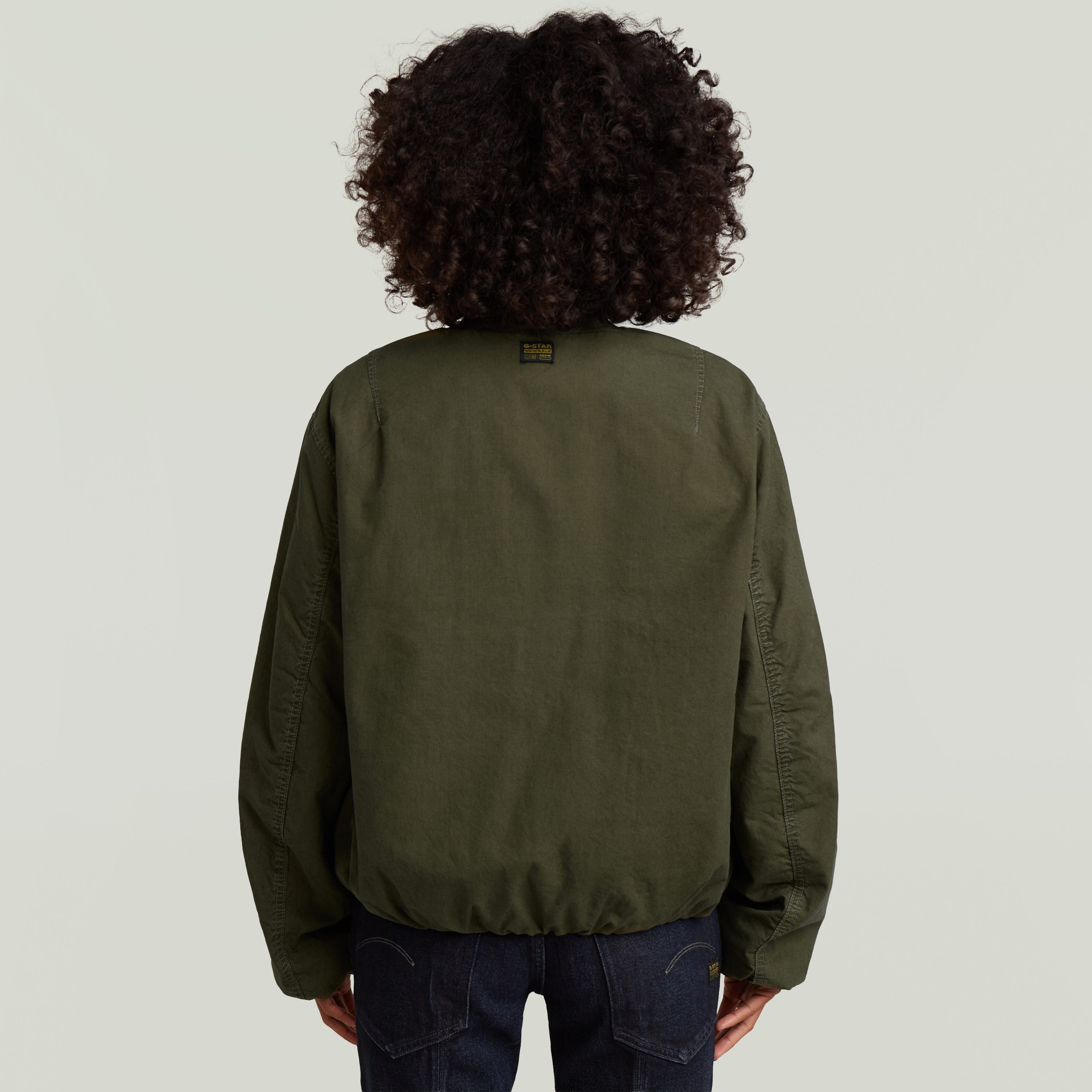 Mujer de espaldas usando una cazadora de aviador padded en color verde con diseño clásico tipo bomber.