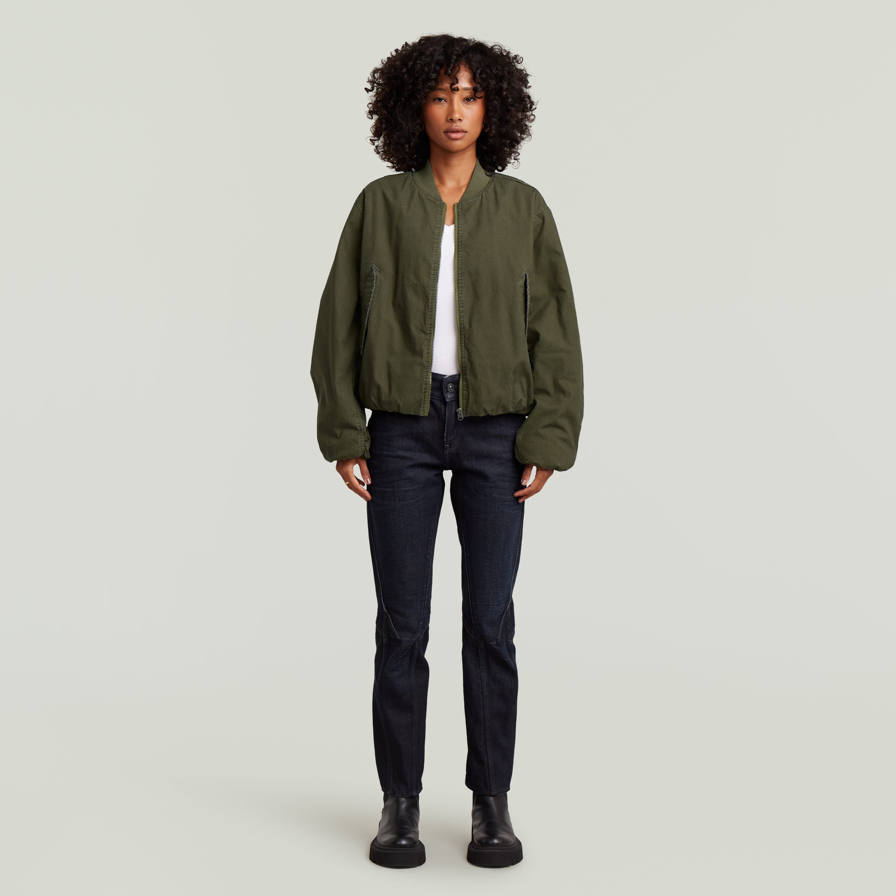 Imagen de mujer usando una cazadora de aviador padded bomber jacket color verde con jeans oscuros.