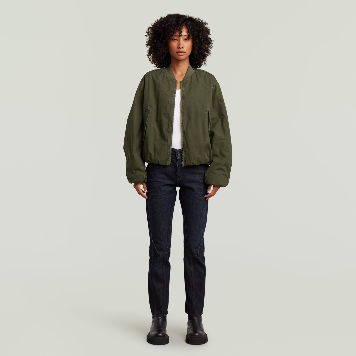 Imagen de mujer usando una cazadora de aviador padded bomber jacket color verde con jeans oscuros.
