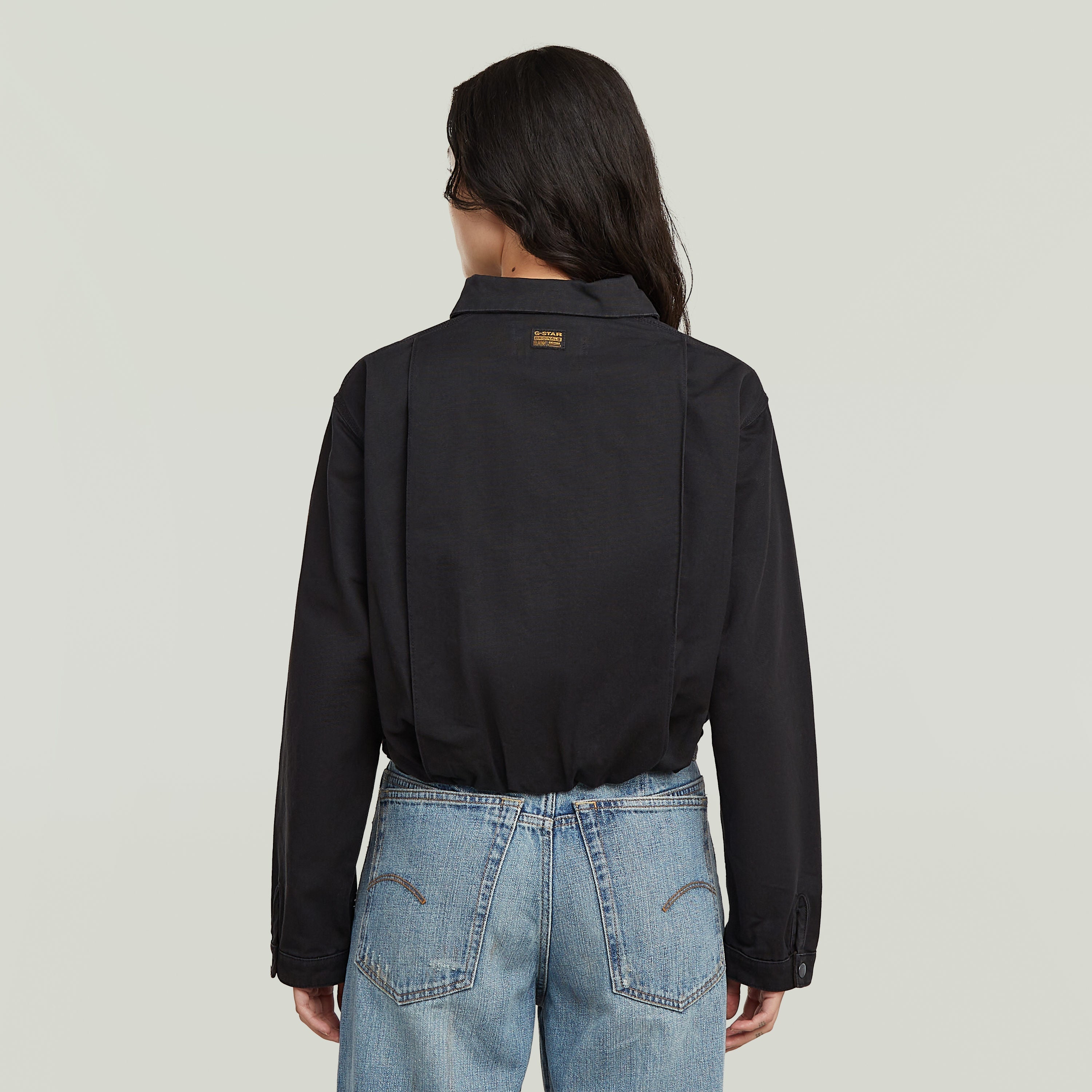 Back view of a woman wearing a black cropped barn jacket with denim jeans.