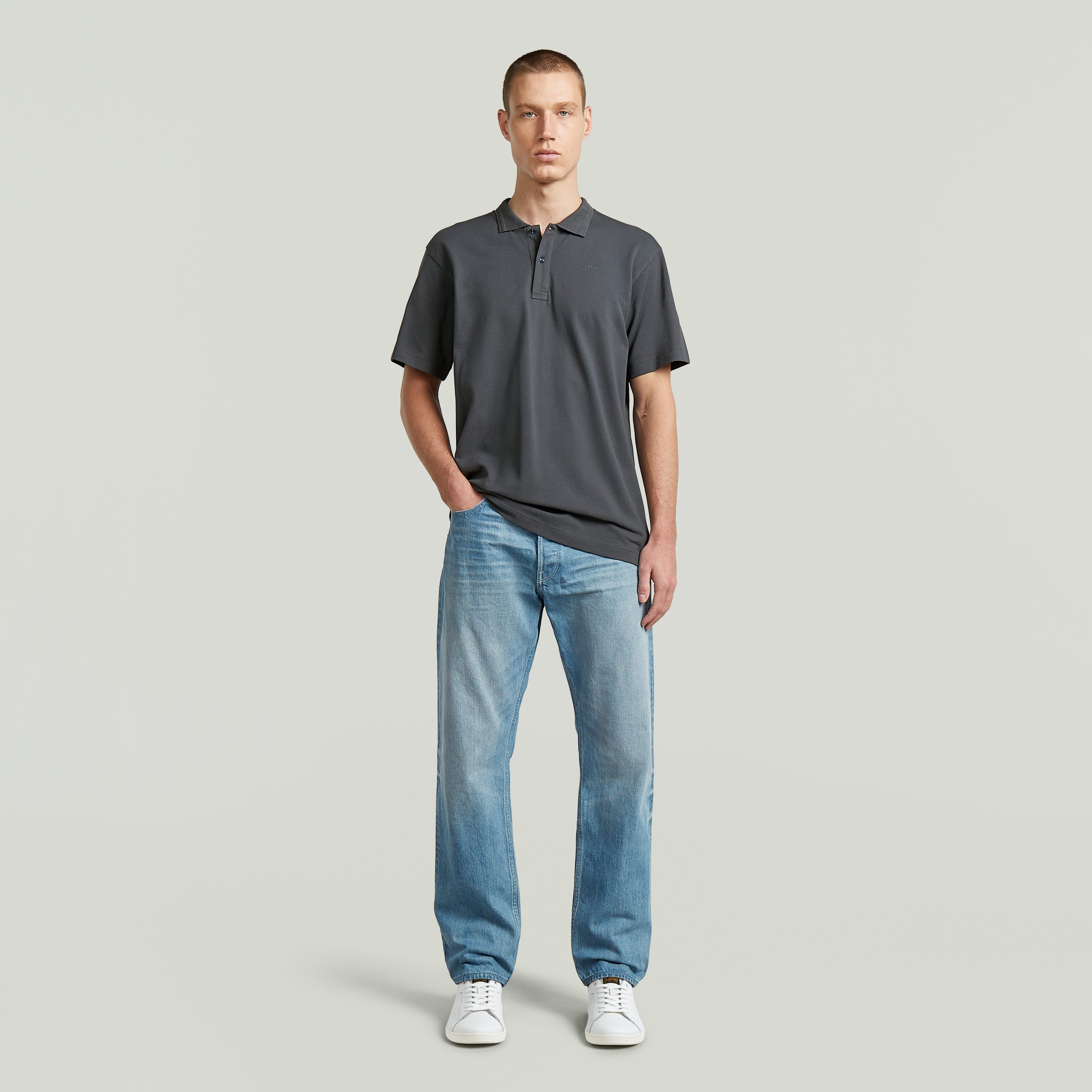 Modelo usando una camisa polo core regular shirt en gris con jeans y zapatillas blancas.