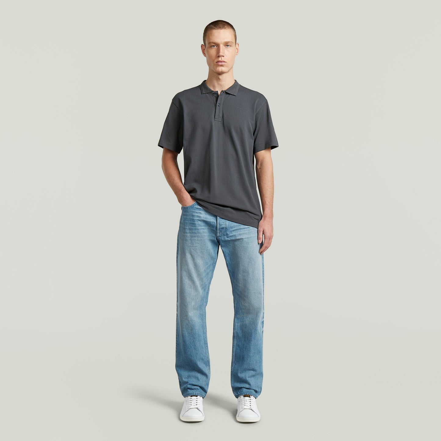 Modelo usando una camisa polo core regular shirt en gris con jeans y zapatillas blancas.