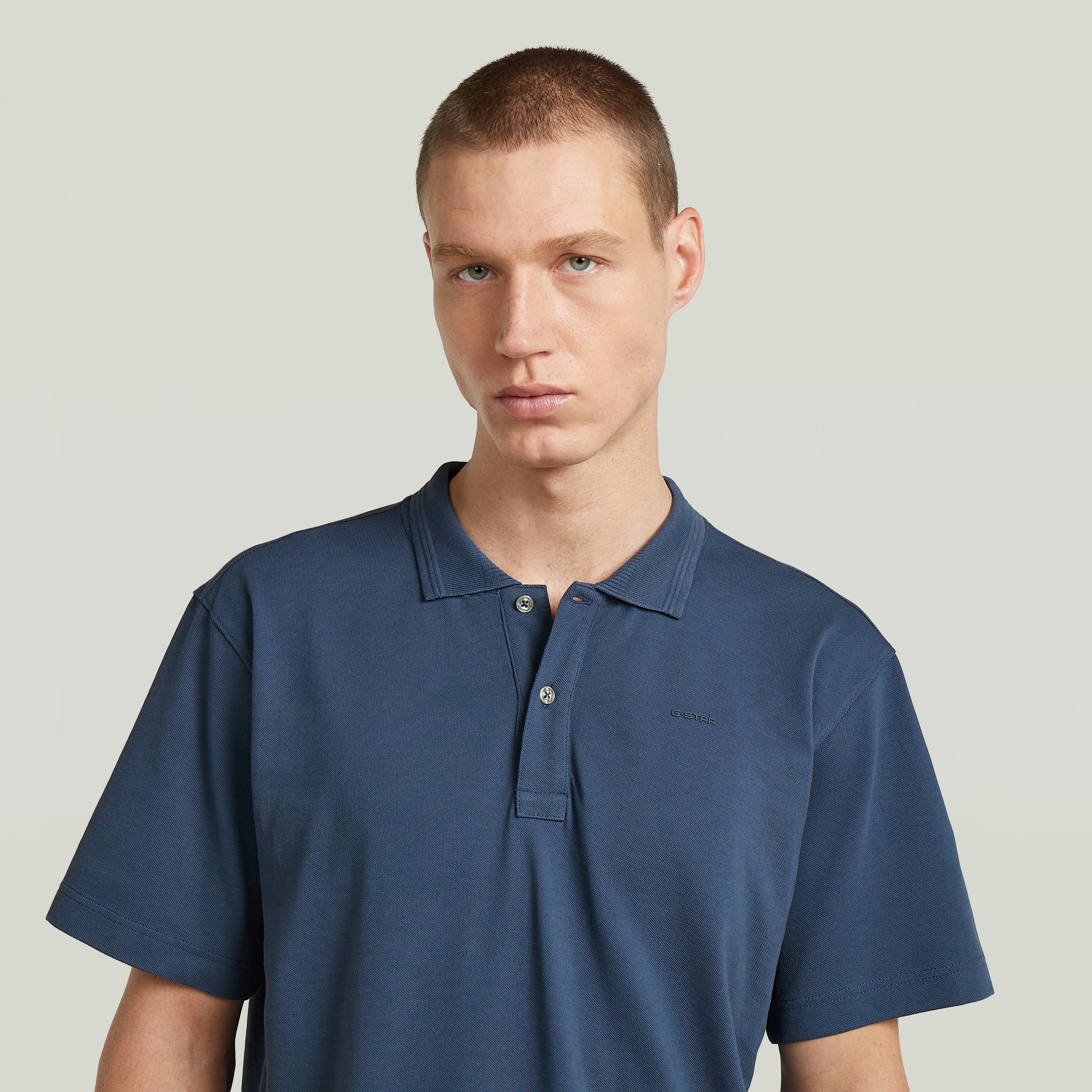 Hombre viste una camisa polo core regular shirt azul intermedio con cuello de polo y cierre de botones.