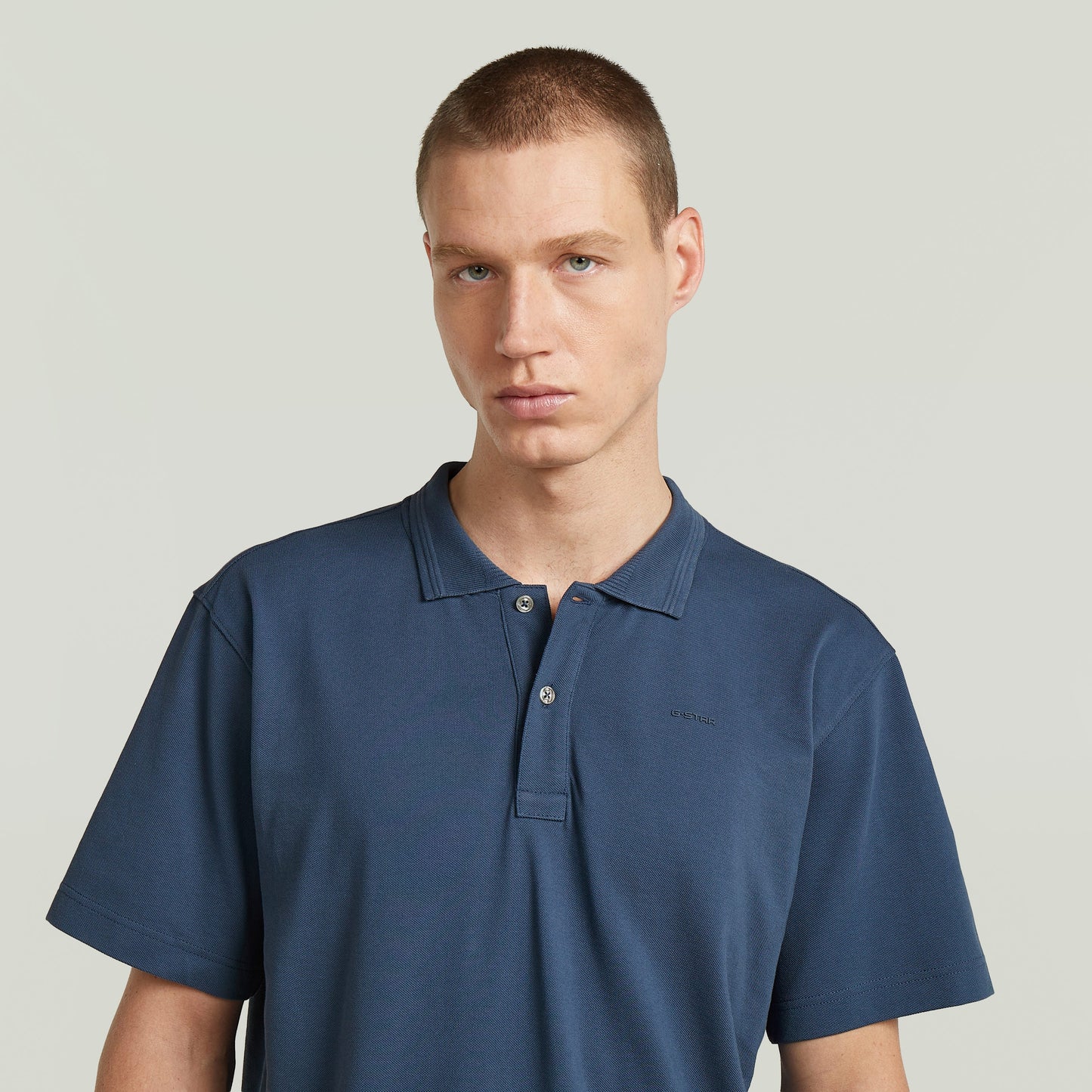 Hombre viste una camisa polo core regular shirt azul intermedio con cuello de polo y cierre de botones.