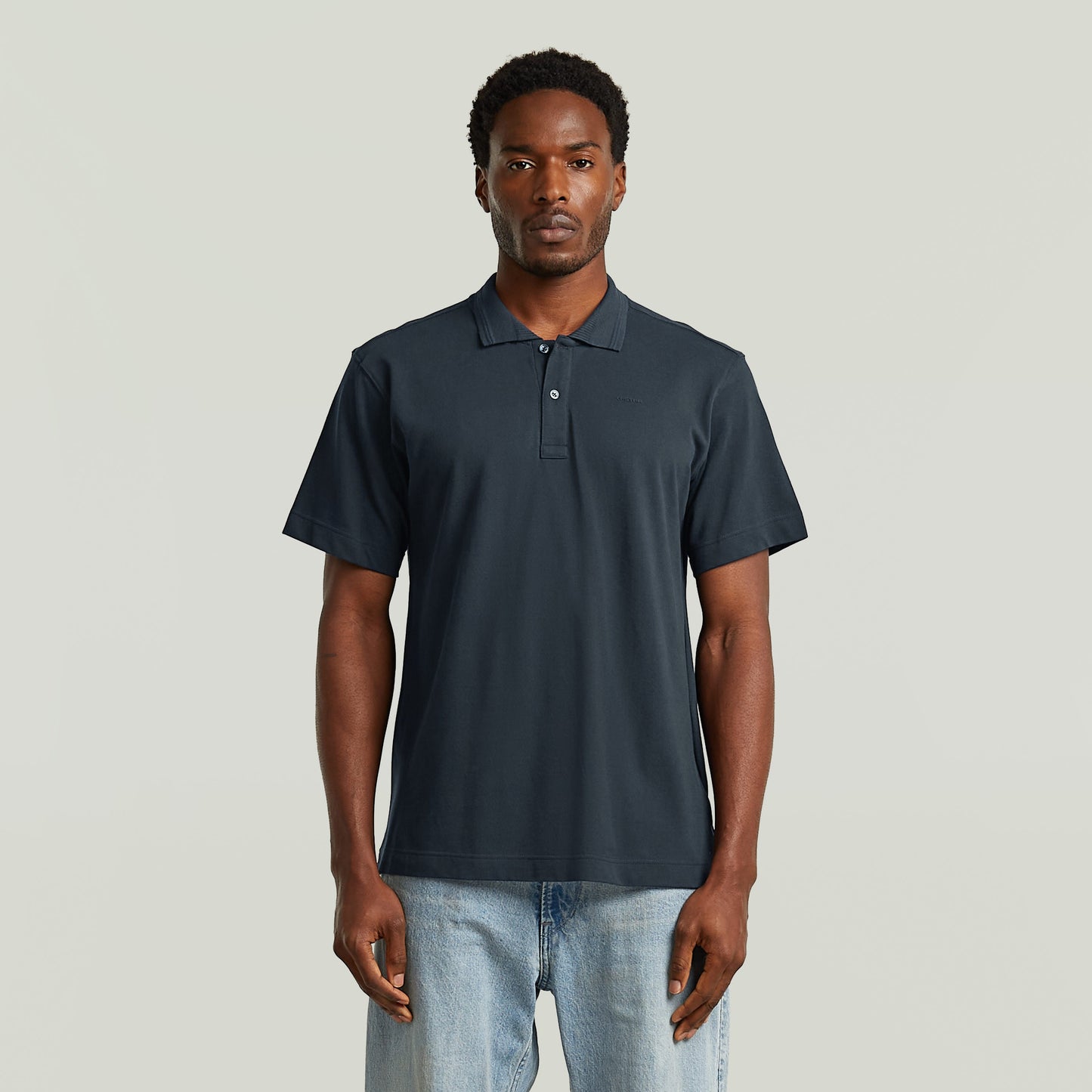 Modelo masculino vistiendo una eco-friendly polo shirt de color azul oscuro con cuello clásico y cierre de botones.