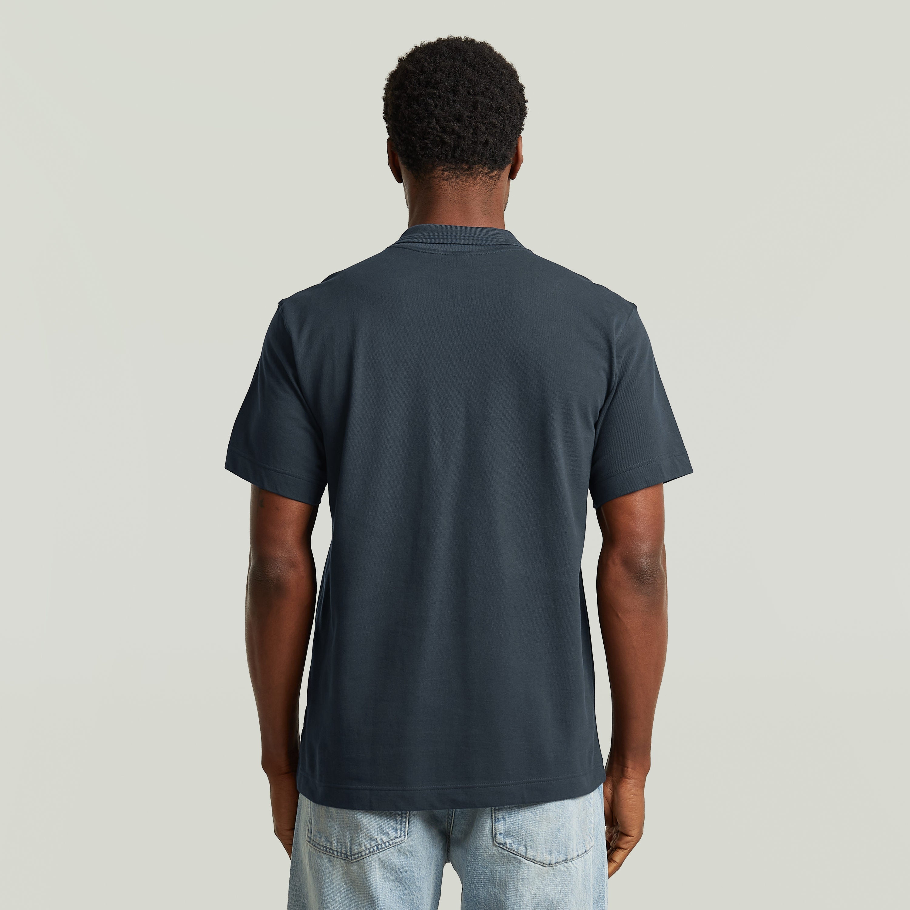 Hombre usando una eco-friendly polo shirt de color azul oscuro, vista trasera, diseño cómodo y elegante.
