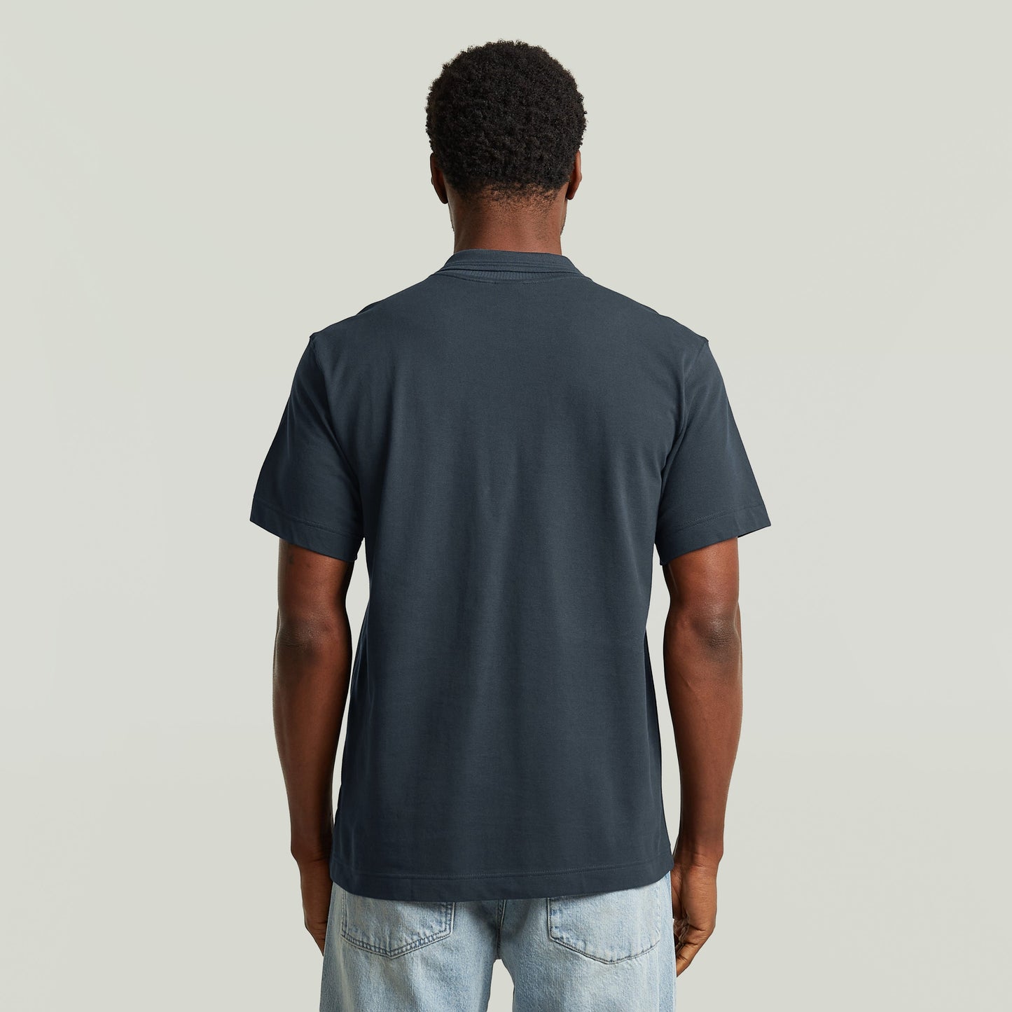 Hombre usando una eco-friendly polo shirt de color azul oscuro, vista trasera, diseño cómodo y elegante.