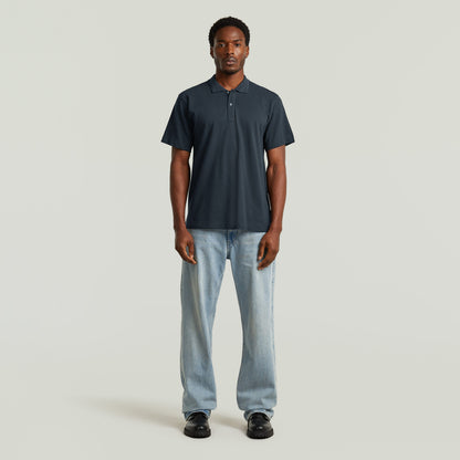 Modelo masculino vistiendo un eco-friendly polo shirt azul oscuro, pantalones de mezclilla y calzado negro.