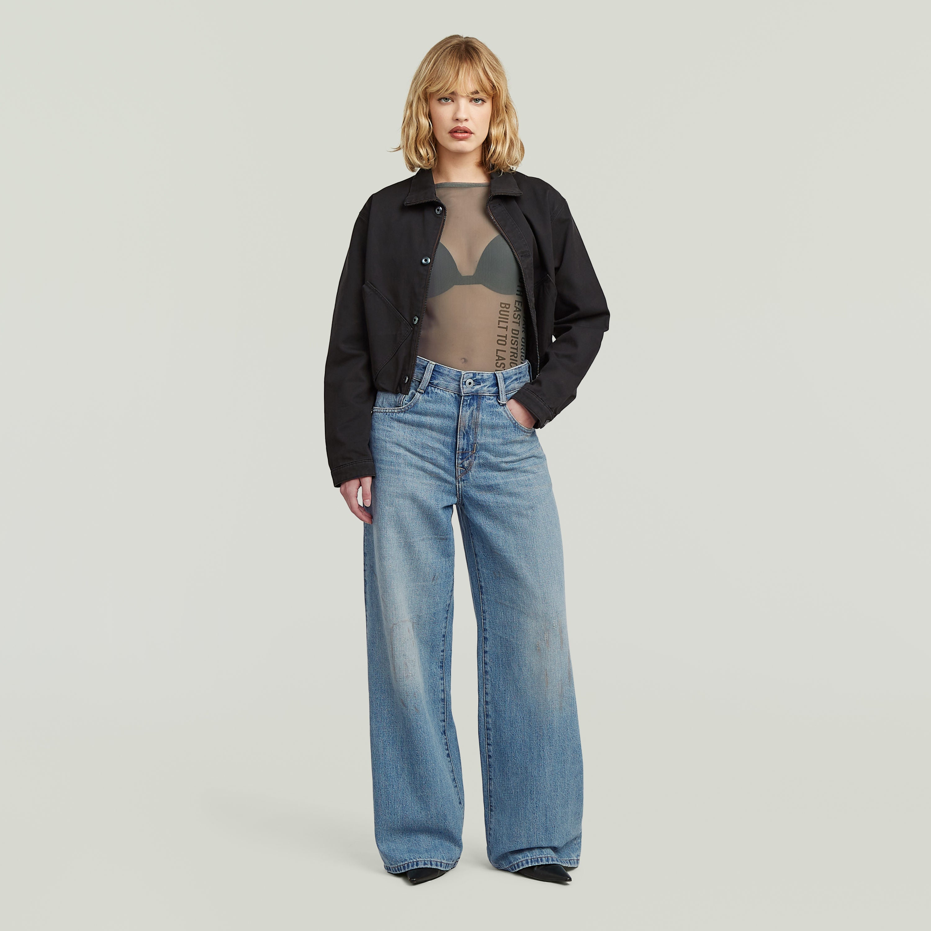 Mujer usando una camiseta slim con detalle gráfico, chaqueta negra y jeans anchos, mirada al frente.