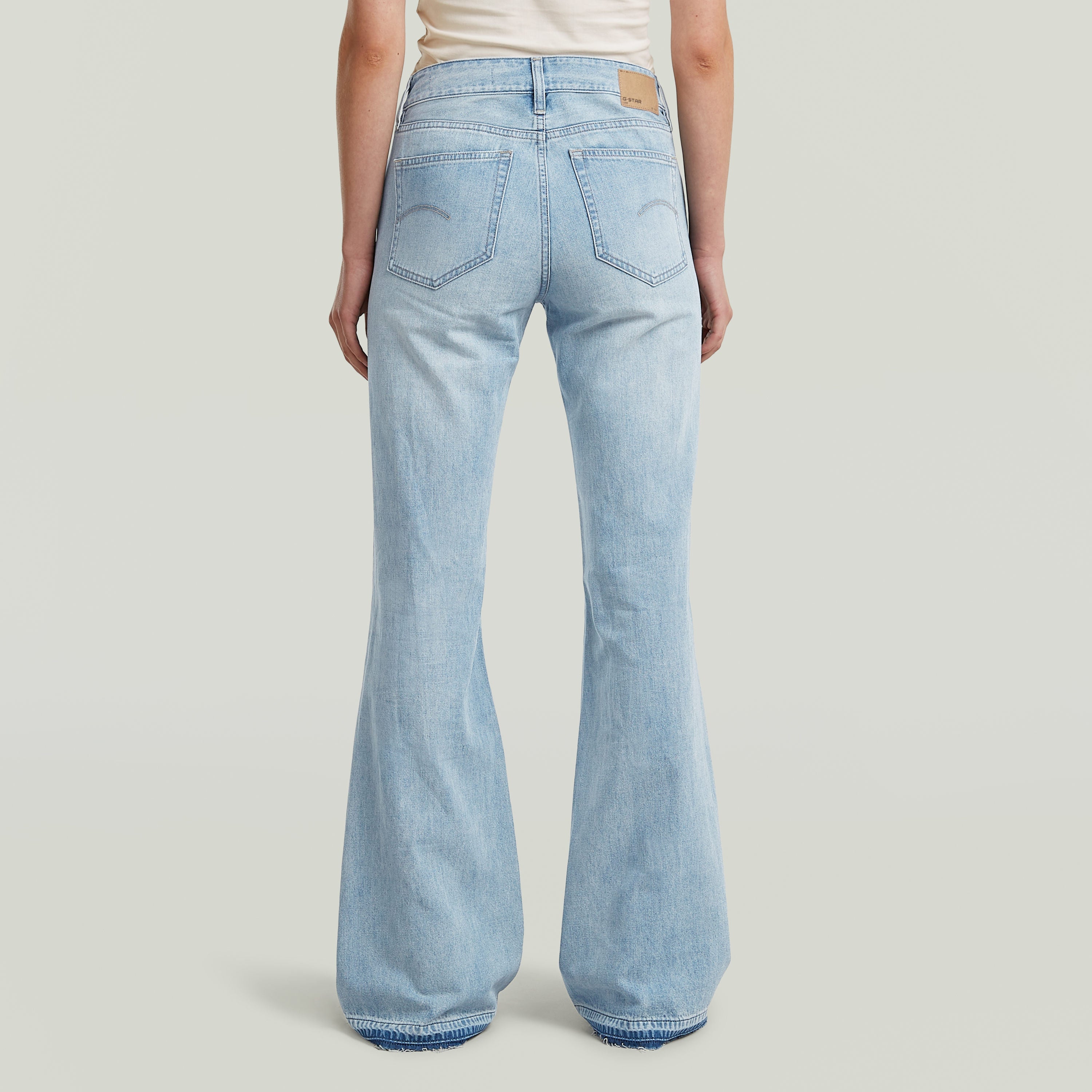 Mujer usando jeans Stevey 3D Flare con corte bootcut en color azul intermedio, vista trasera.