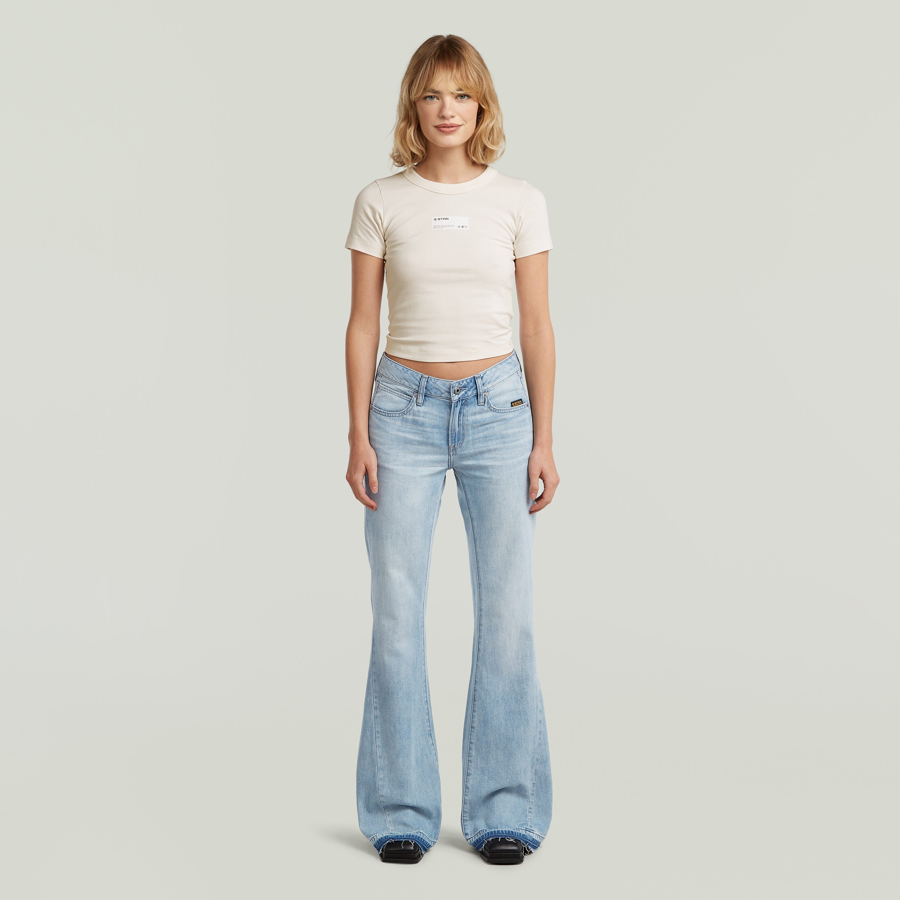 Mujer luciendo jeans Stevey 3D Flare, estilo bootcut en color azul intermedio, 100% algodón.