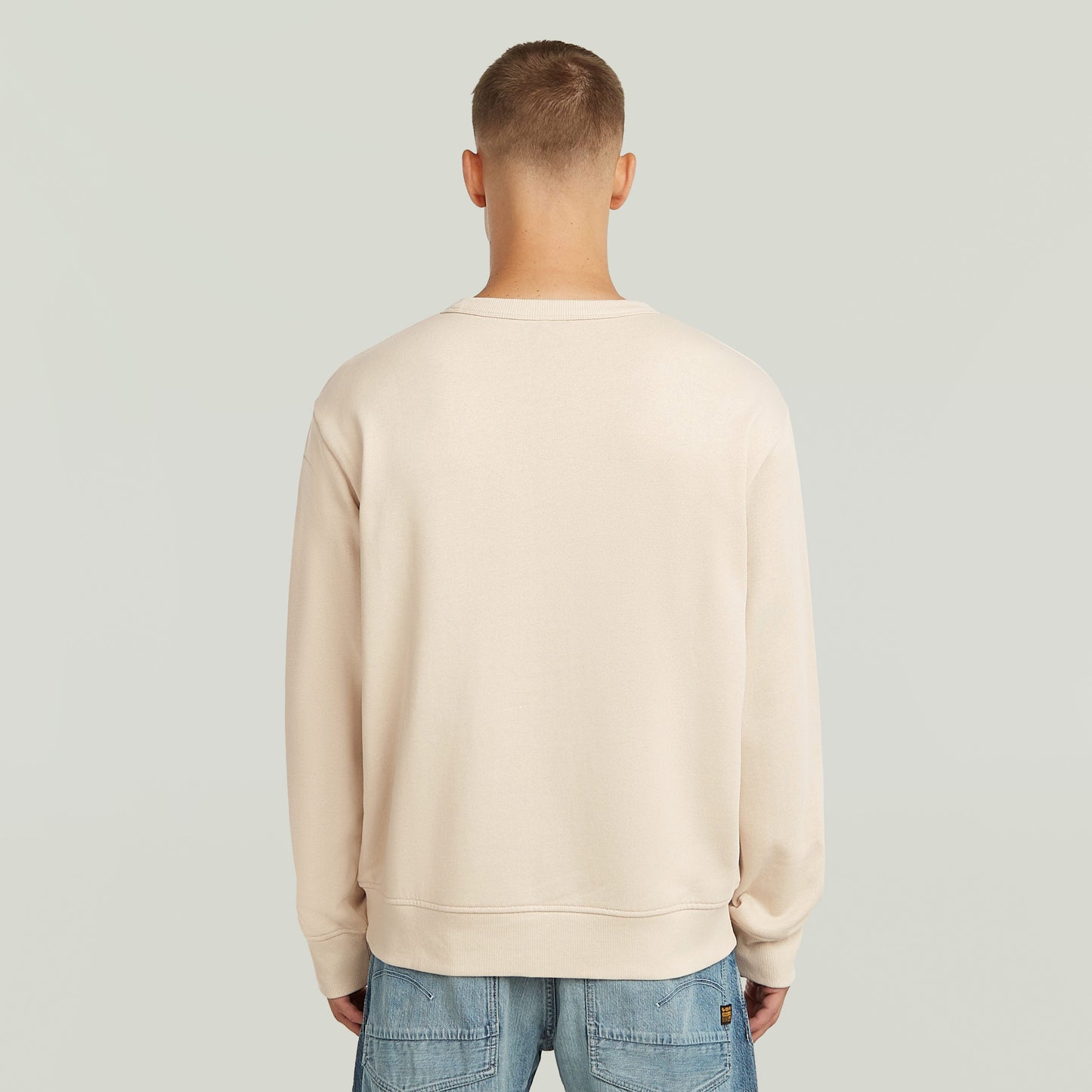 Hombre vistiendo una sudadera con logotipo de los 90, vista trasera, color crema, diseño clásico y cortado regular.