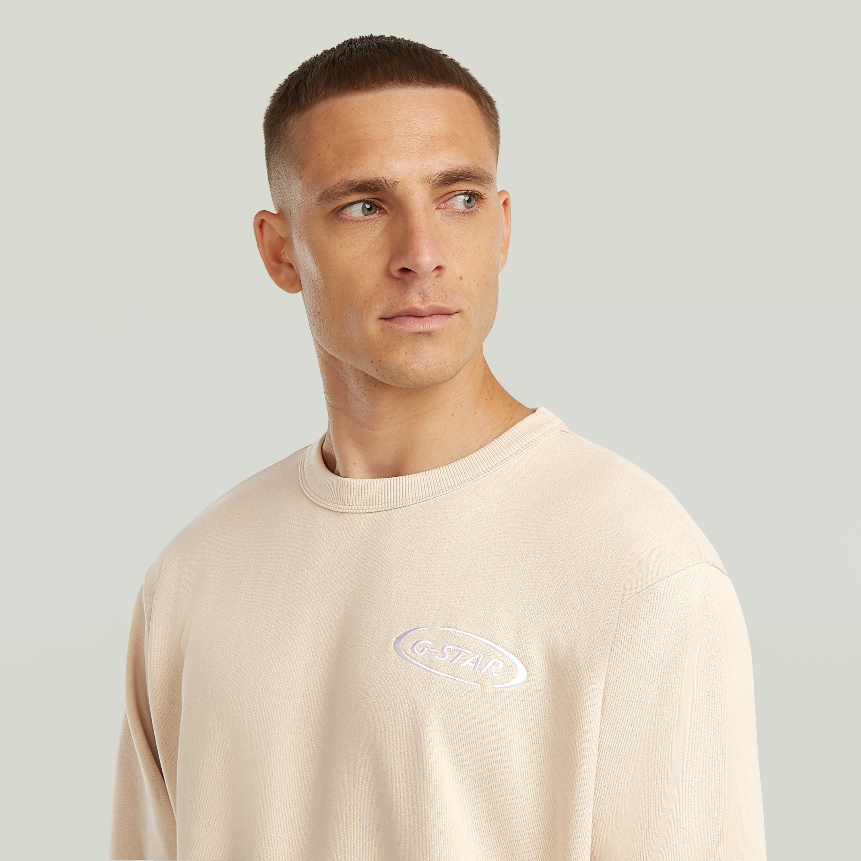 Hombre usando una sudadera con logotipo de los 90 en color beige con cuello redondo y diseño clásico.