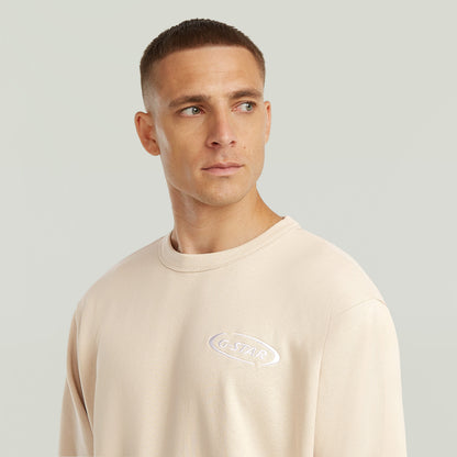 Hombre usando una sudadera con logotipo de los 90 en color beige con cuello redondo y diseño clásico.