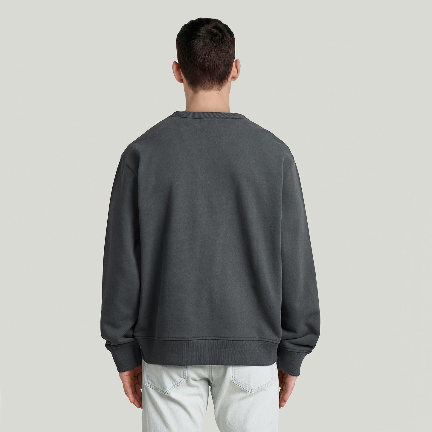 Hombre usando sudadera con logotipo de los 90, vista trasera, color gris, corte regular y cuello redondo.
