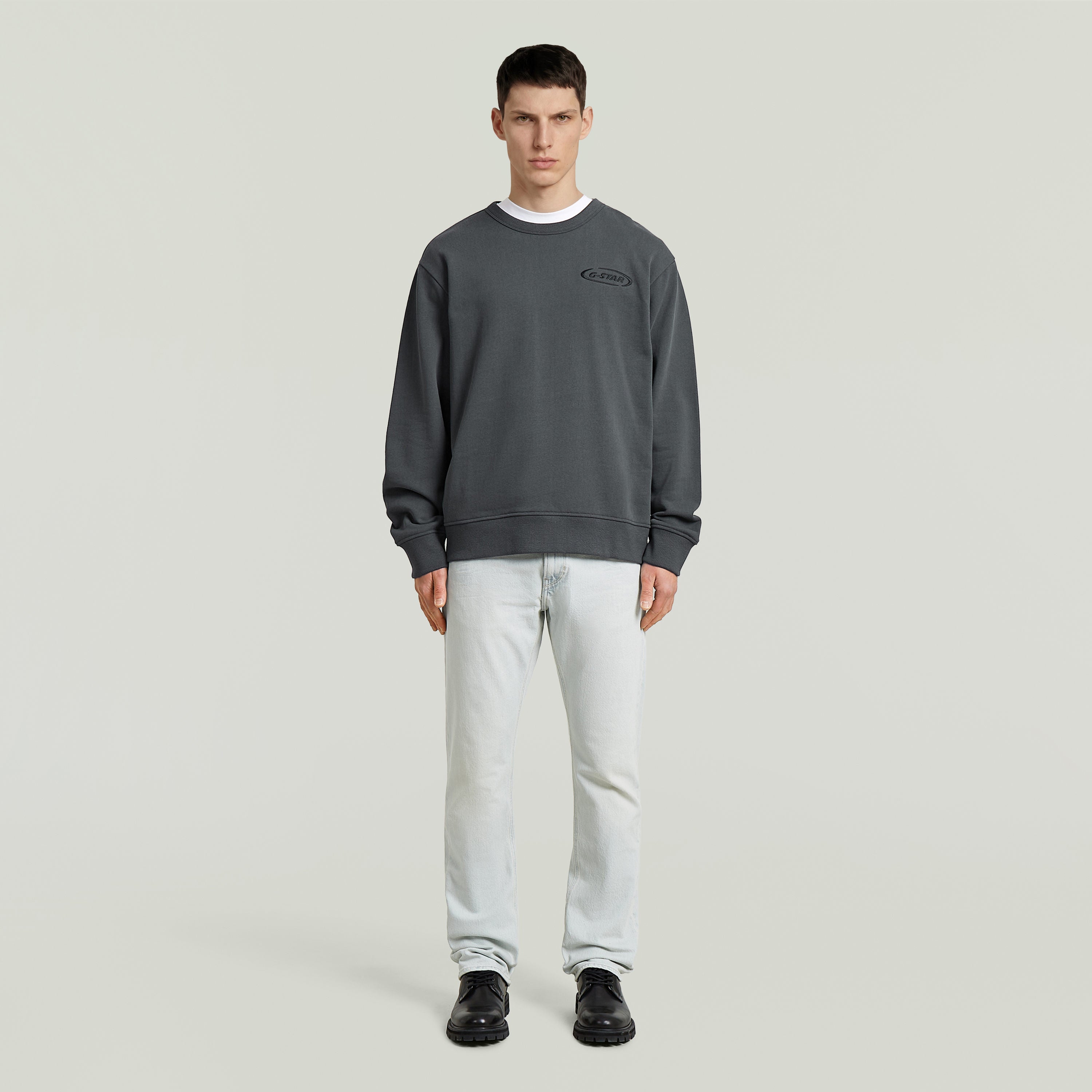 Sudadera con logotipo de los 90 en color gris, corte regular y cuello redondo, modelo masculino con jeans.