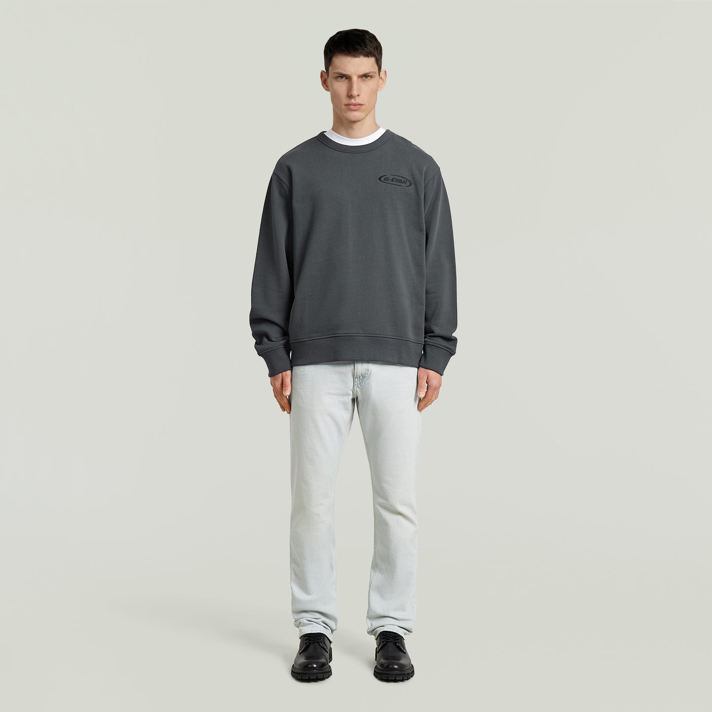 Sudadera con logotipo de los 90 en color gris, corte regular y cuello redondo, modelo masculino con jeans.
