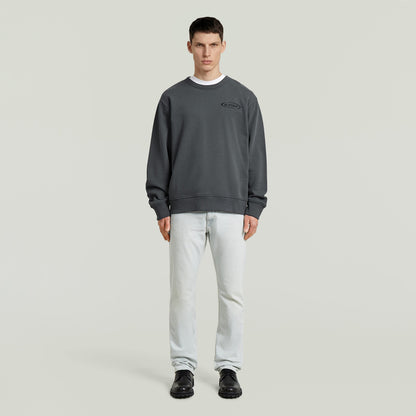 Sudadera con logotipo de los 90 en color gris, corte regular y cuello redondo, modelo masculino con jeans.