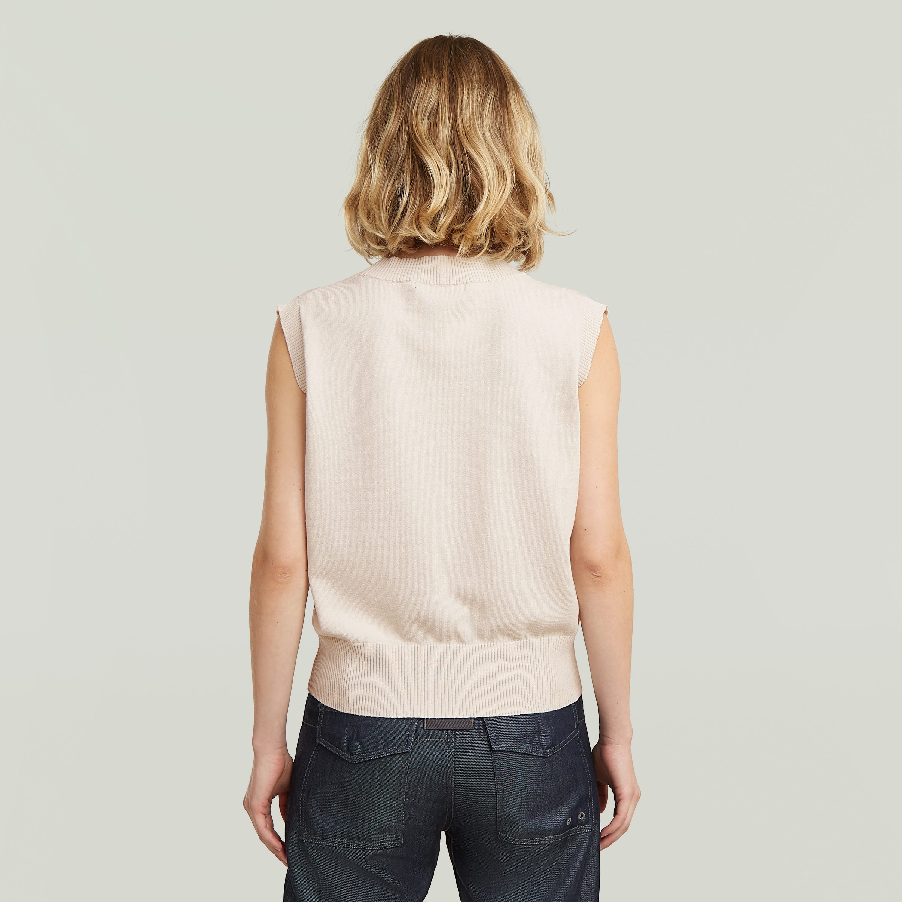 Mujer vista trasera usando un chaleco de punto holgado en color blanco, diseño sin mangas y cómodo.