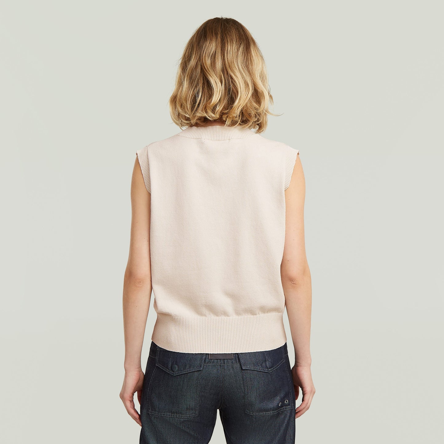Mujer vista trasera usando un chaleco de punto holgado en color blanco, diseño sin mangas y cómodo.