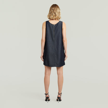 Mujer de espaldas usando un vestido cargo shift ligero en denim oscuro, con tirantes anchos y cierre de cremallera.