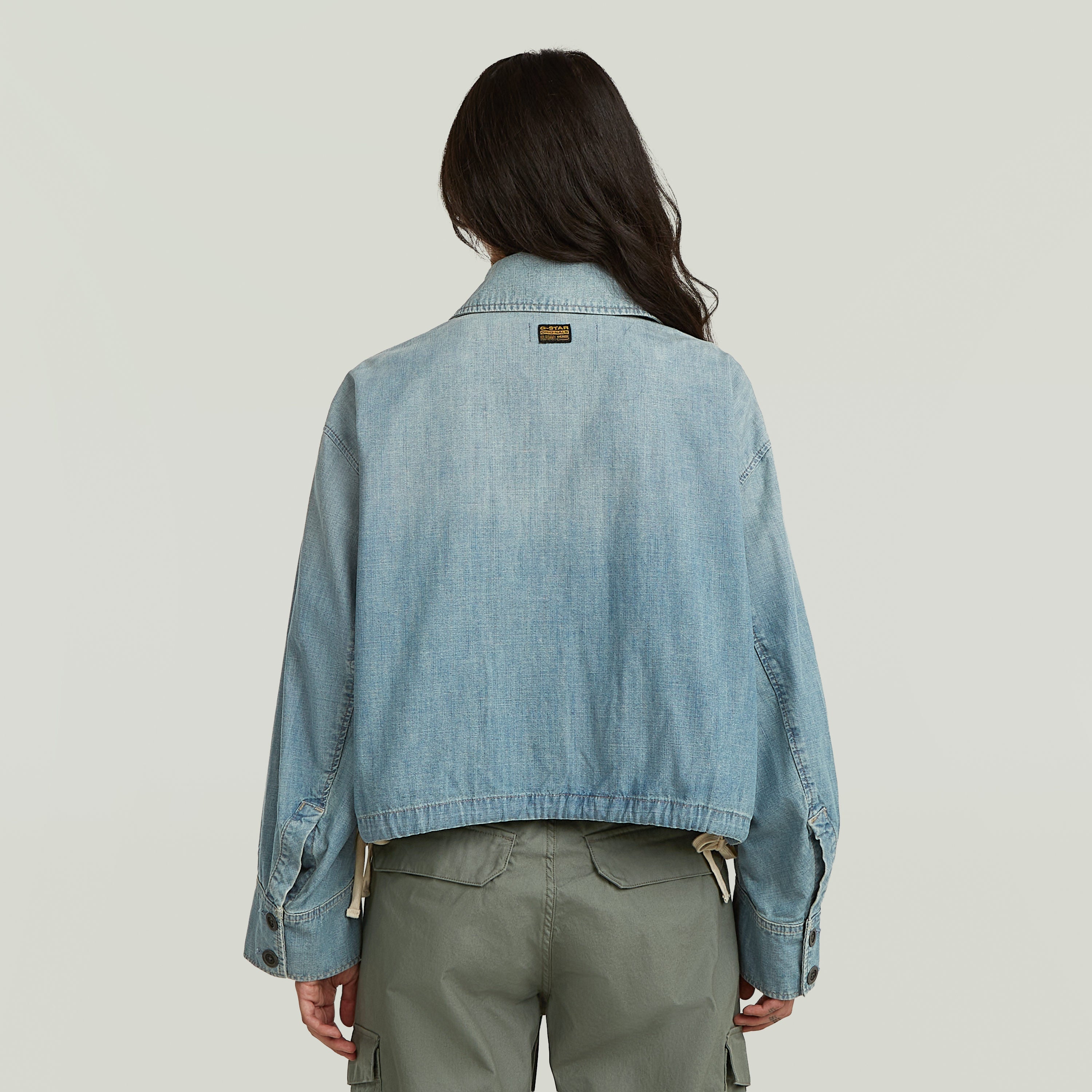 Mujer de espaldas usando chaqueta parachute oversized color azul claro con diseño extragrande y cuello clásico.
