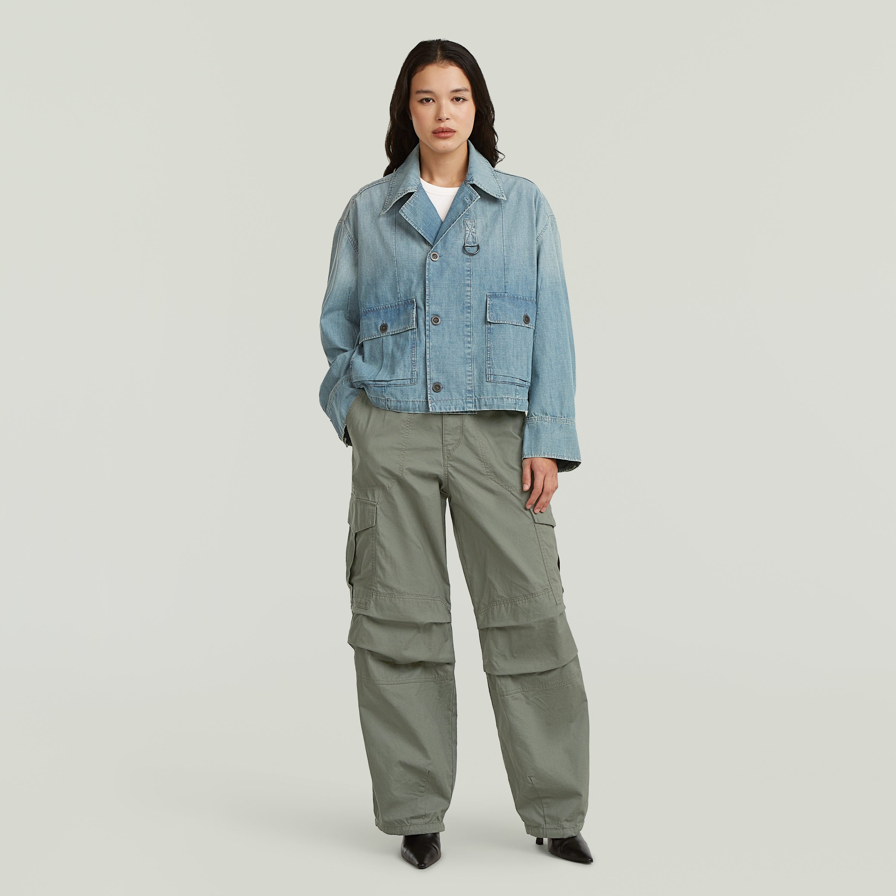 Modelo con chaqueta parachute oversized de mezclilla azul claro y pantalones cargo verdes.
