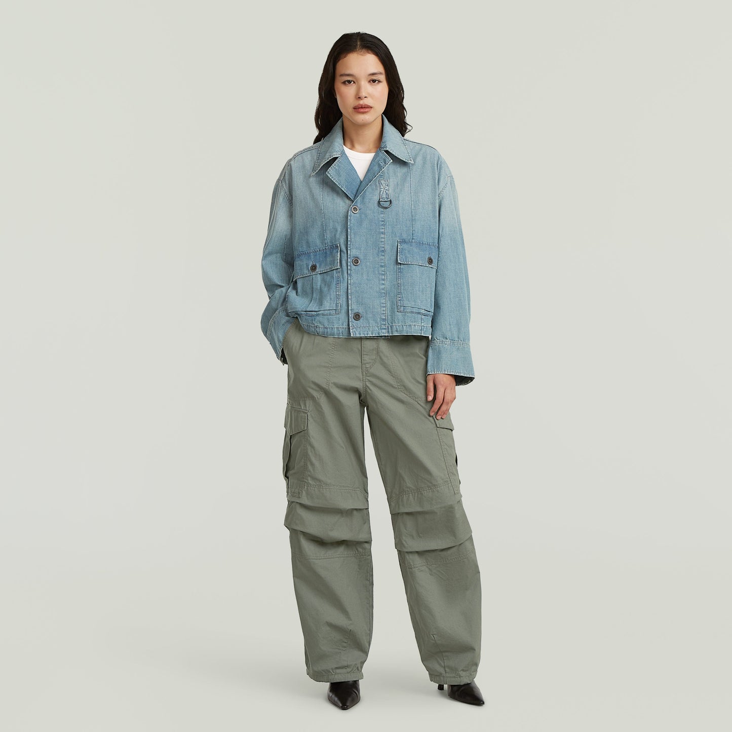 Modelo con chaqueta parachute oversized de mezclilla azul claro y pantalones cargo verdes.