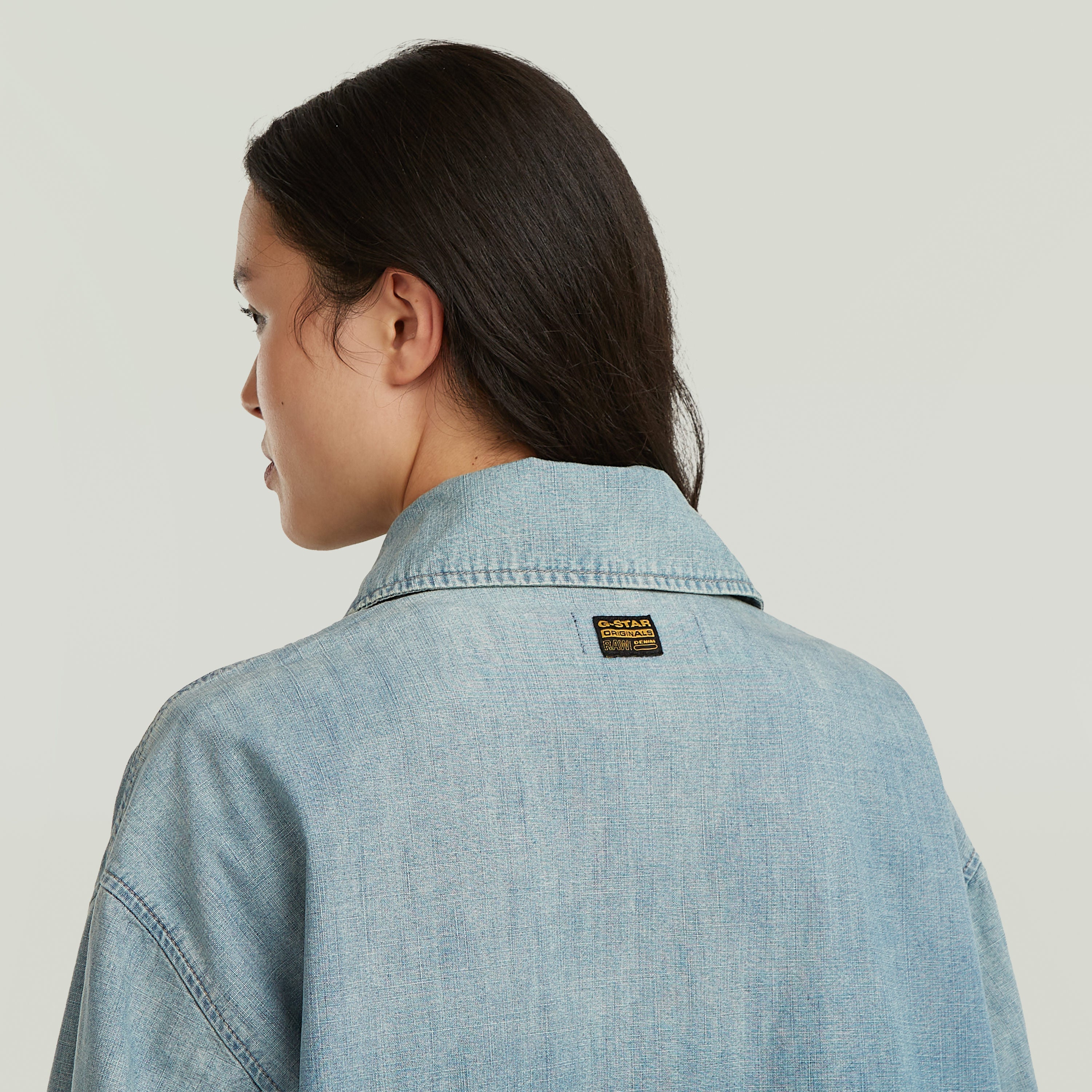 Mujer usando chaqueta parachute oversized con parche de G-STAR en la parte trasera, color azul claro.