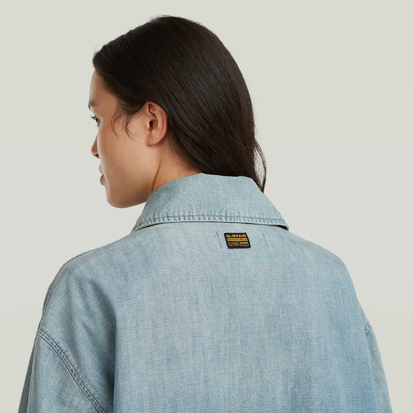 Mujer usando chaqueta parachute oversized con parche de G-STAR en la parte trasera, color azul claro.