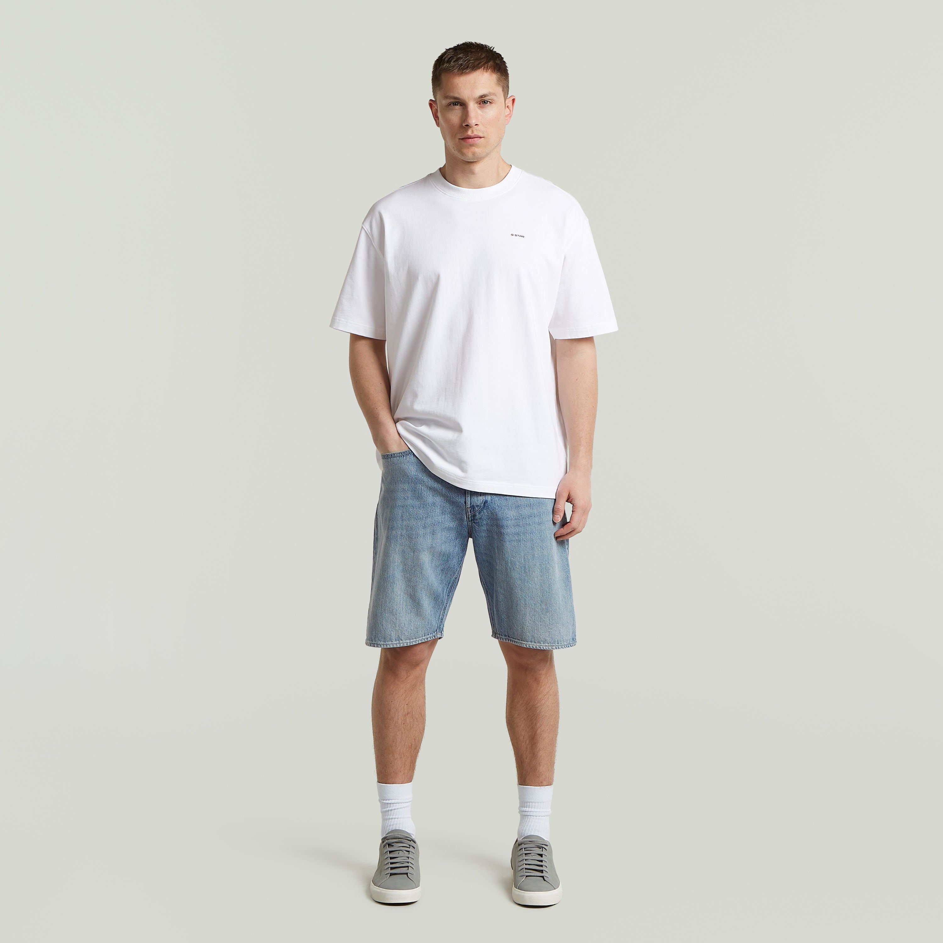Hombre con camiseta blanca y pantalones cortos, vistiendo una relaxed fit graphic tee y zapatillas. Estilo moderno.