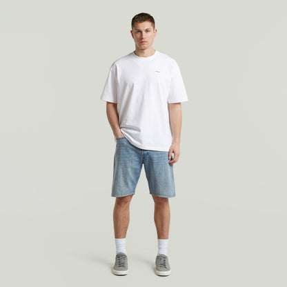 Hombre con camiseta blanca y pantalones cortos, vistiendo una relaxed fit graphic tee y zapatillas. Estilo moderno.