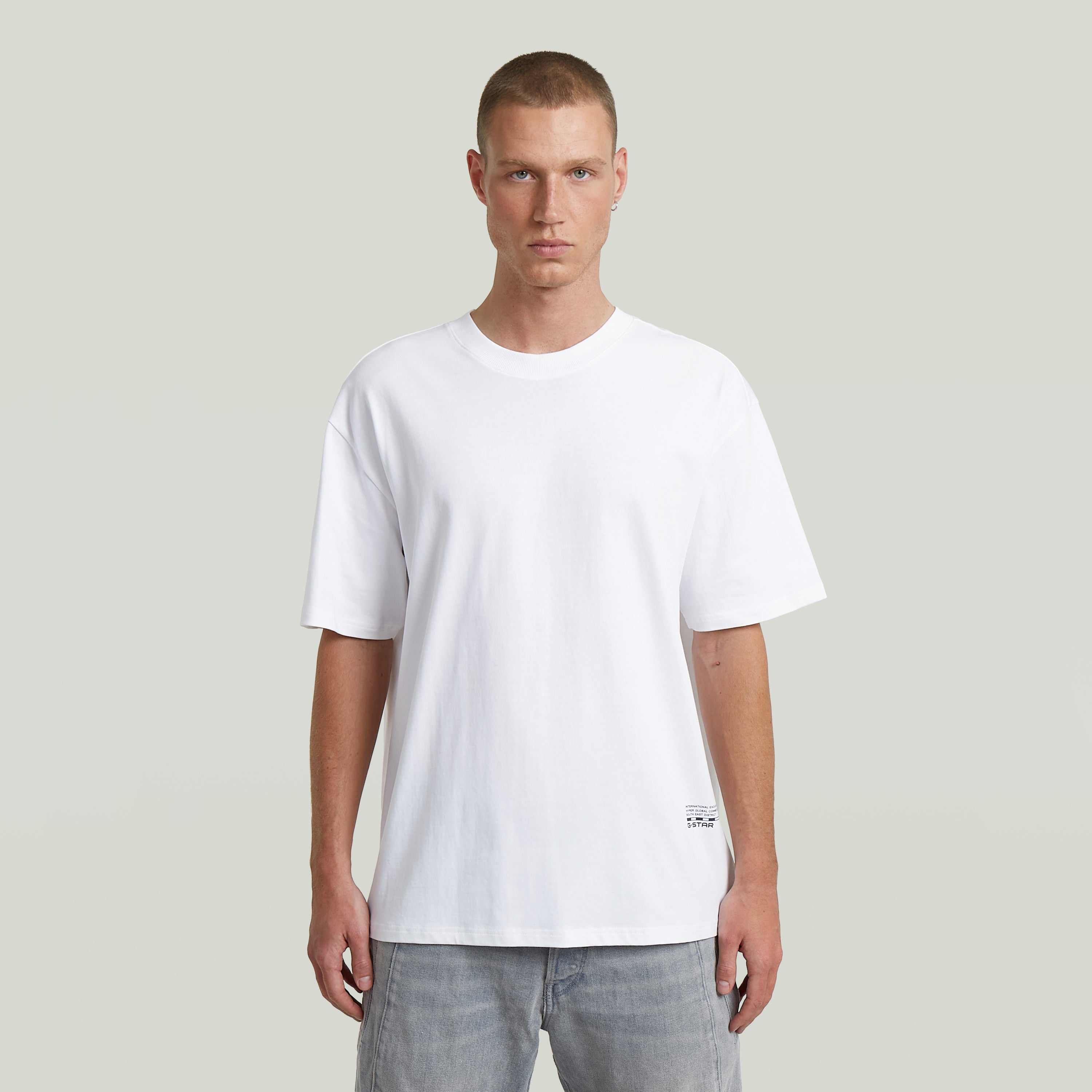 Modelo masculino luciendo la camiseta Back Applique Relaxed, blanca, de corte relajado y cuello redondo.