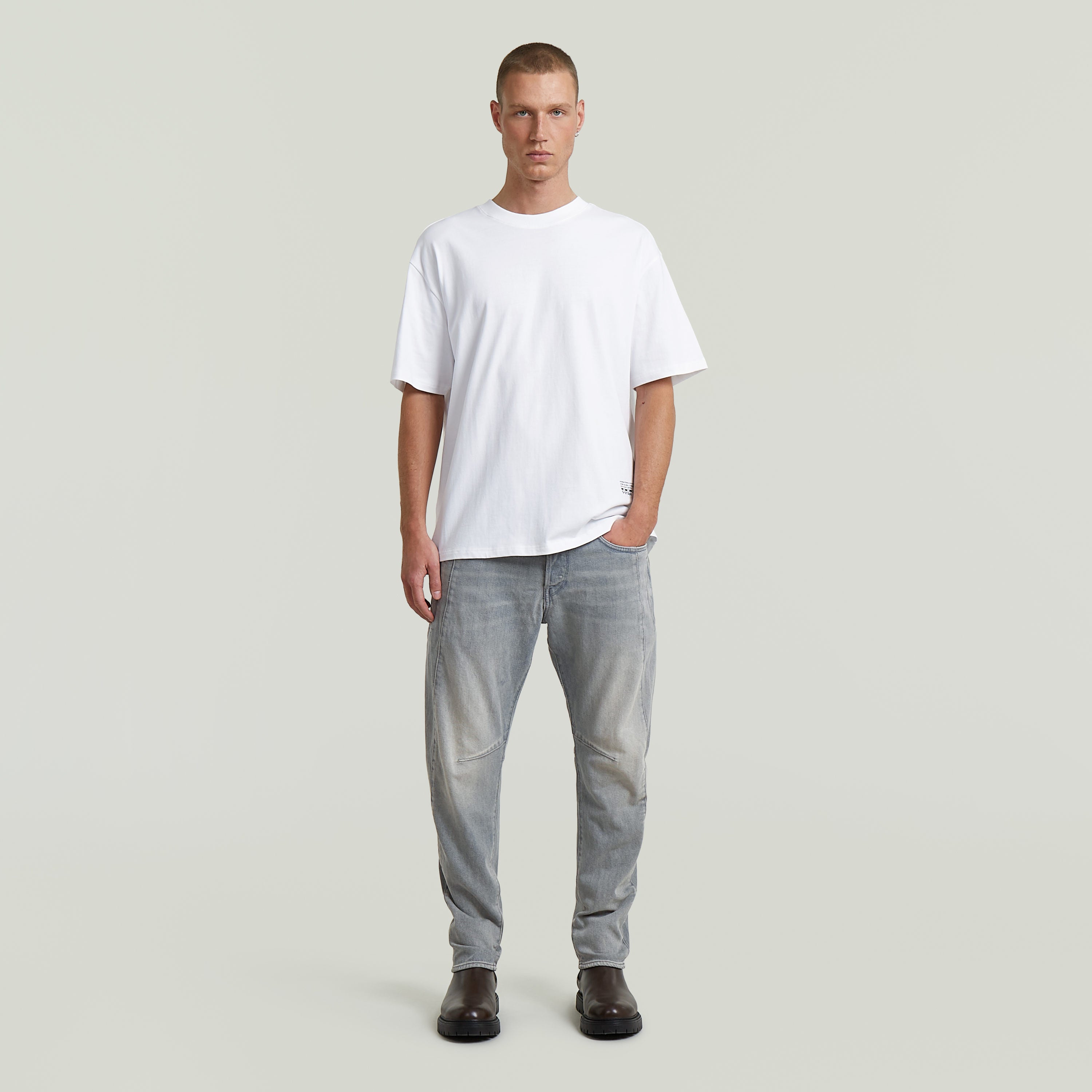 Hombre usando camiseta Back Applique Relaxed blanca con jeans gris claro, estilo casual.