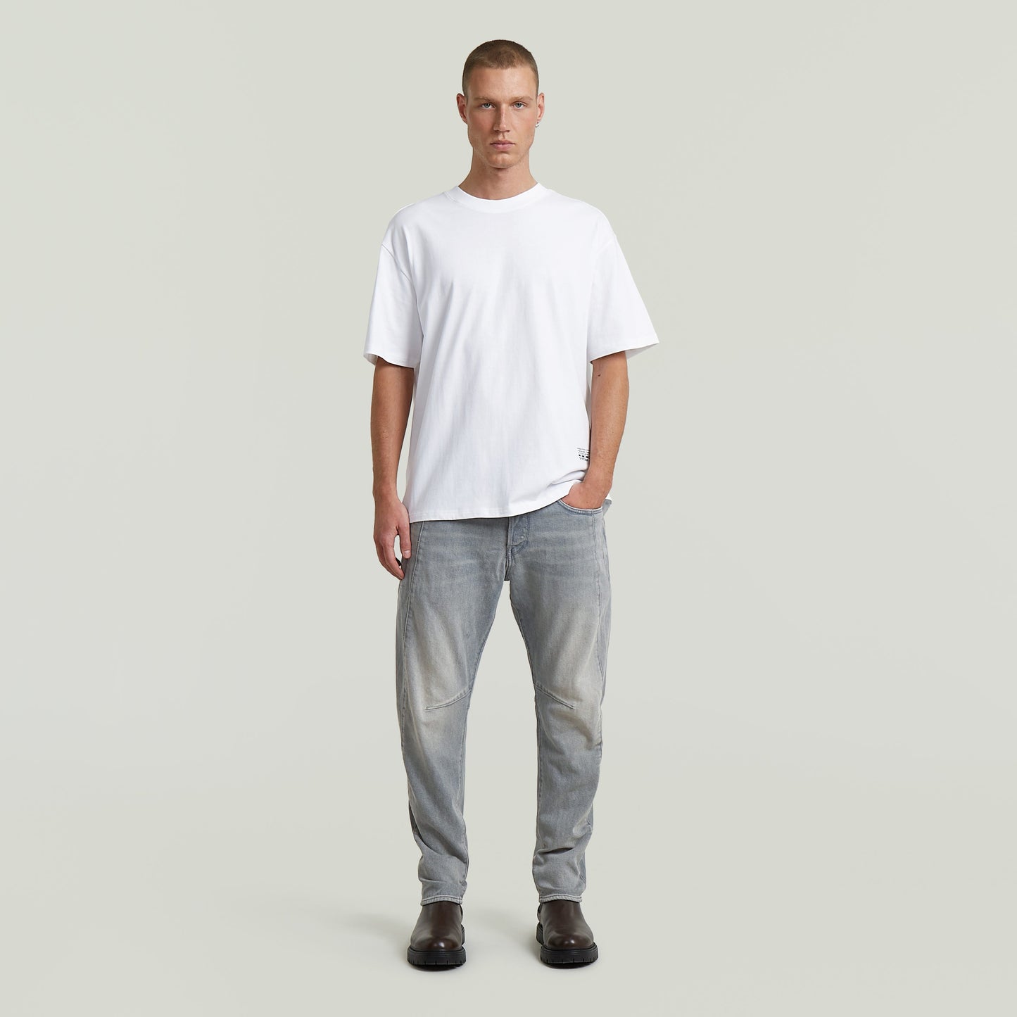 Hombre usando camiseta Back Applique Relaxed blanca con jeans gris claro, estilo casual.