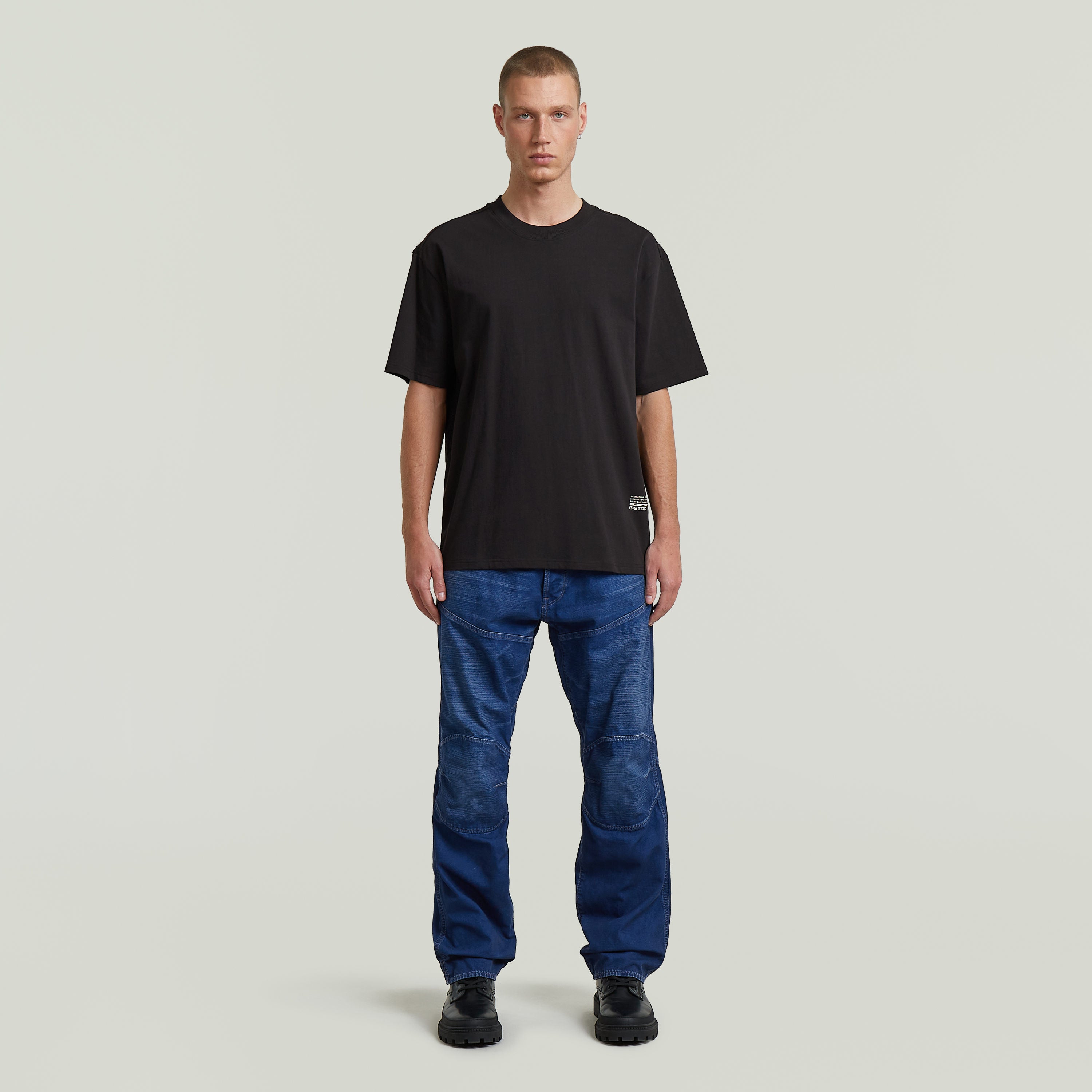 Hombre usando camiseta negra, modelo relaxed back applique t-shirt, con jeans azul y fondo neutro.