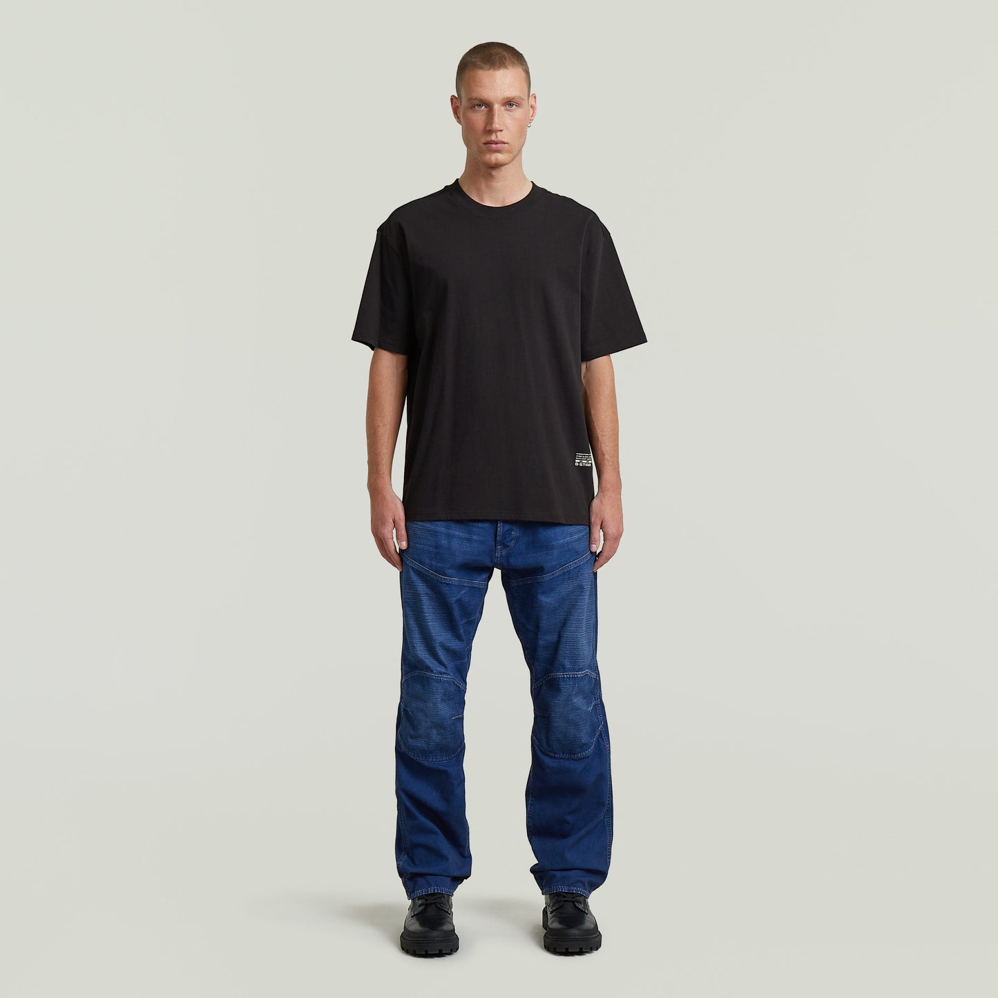 Hombre usando camiseta negra, modelo relaxed back applique t-shirt, con jeans azul y fondo neutro.