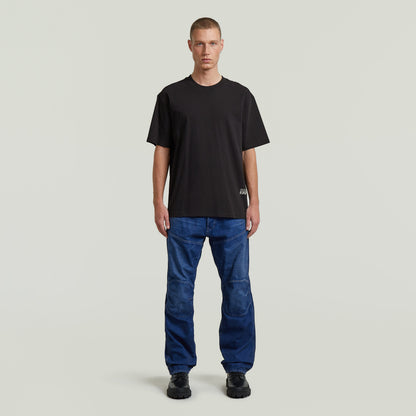 Hombre usando camiseta negra, modelo relaxed back applique t-shirt, con jeans azul y fondo neutro.
