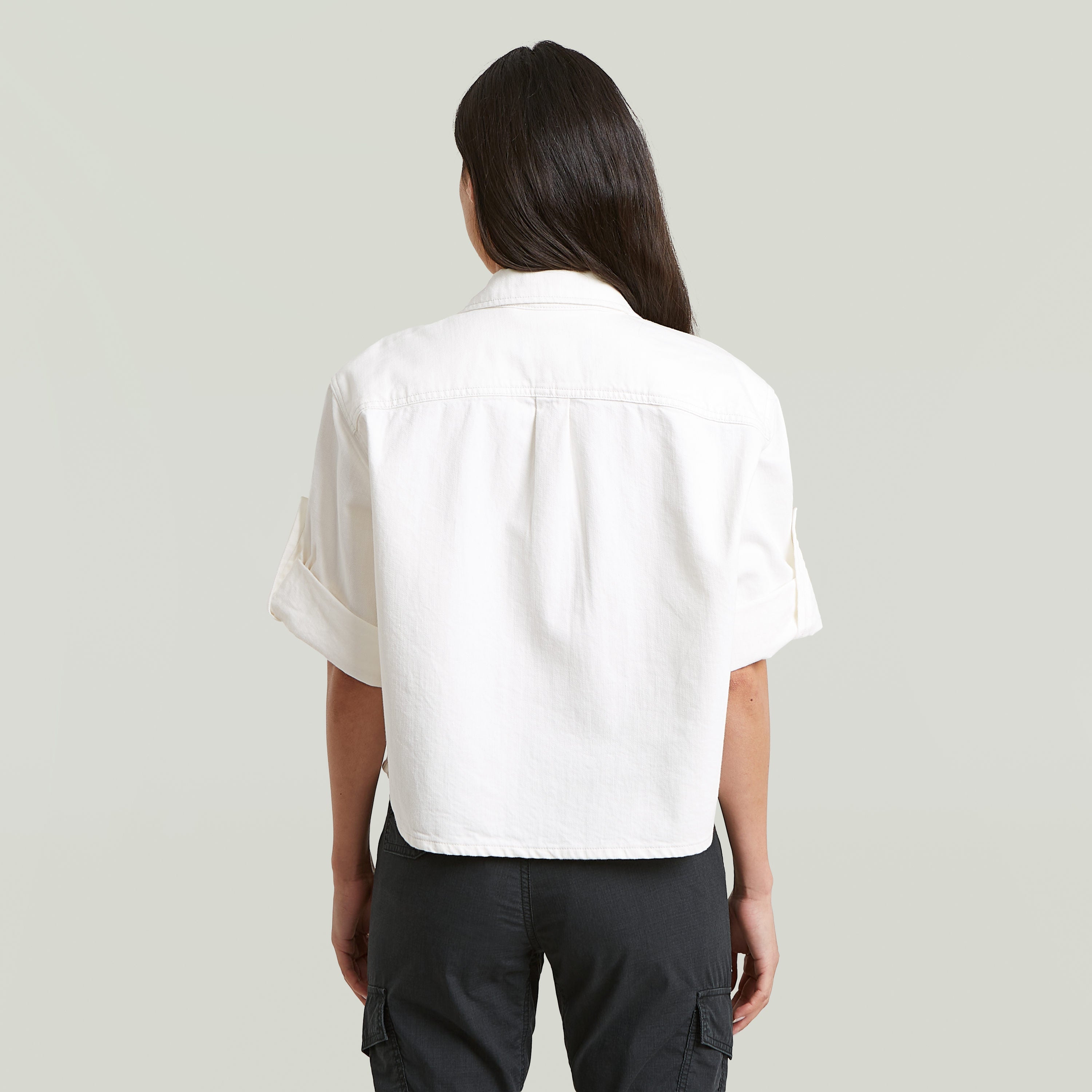 Mujer usando una camisa boxy relaxed fit, vista desde atrás, color blanco, con manga corta y corte relajado.