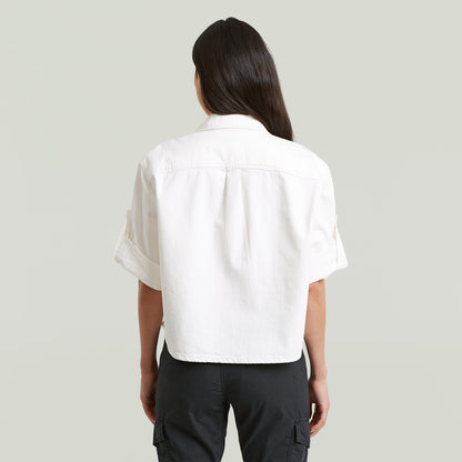 Mujer usando una camisa boxy relaxed fit, vista desde atrás, color blanco, con manga corta y corte relajado.