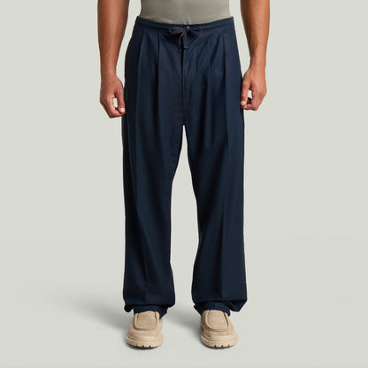 Chino con plisado doble en color azul oscuro, detalle de ajuste cónico y cintura media, con diseño moderno y clásico.