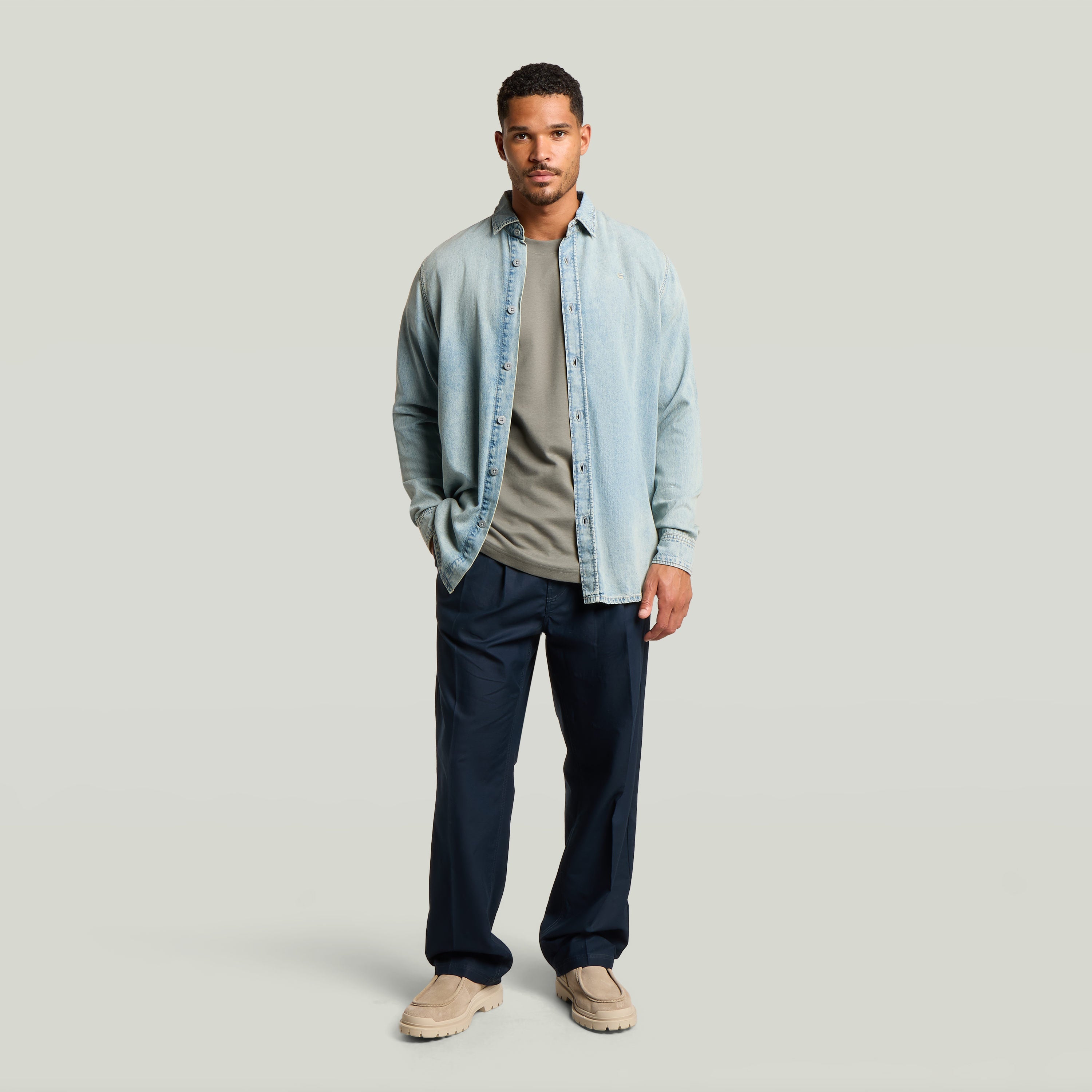 Hombre vistiendo chino con plisado doble, camisa de mezclilla y camiseta, look moderno en color azul oscuro.