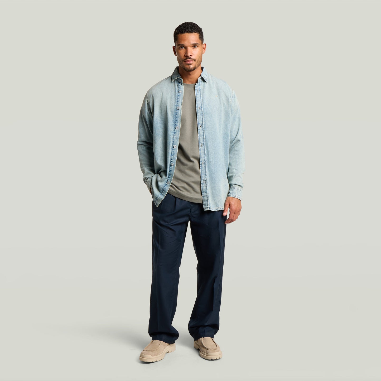 Hombre vistiendo chino con plisado doble, camisa de mezclilla y camiseta, look moderno en color azul oscuro.
