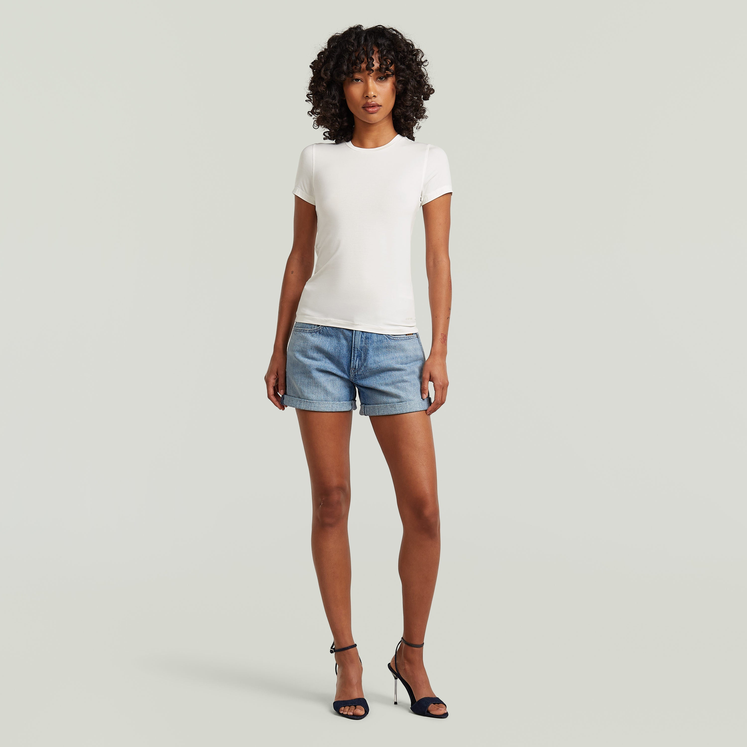 Mujer luciendo camiseta ajustada de modal blanca con shorts de mezclilla y sandalias de tacón.