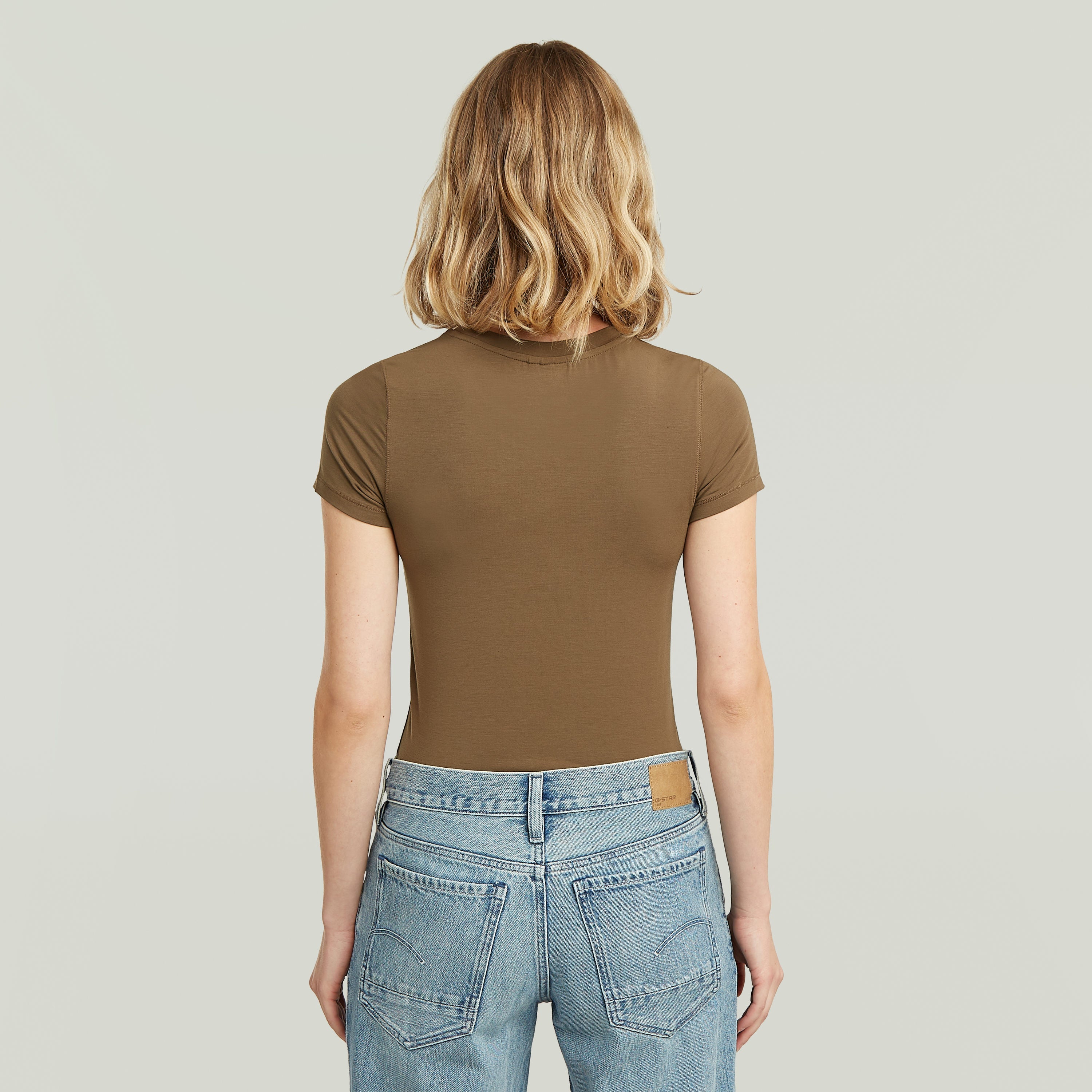 Mujer de espaldas usando una ajustada camiseta de modal marrón con diseño elegante y corte cómodo.