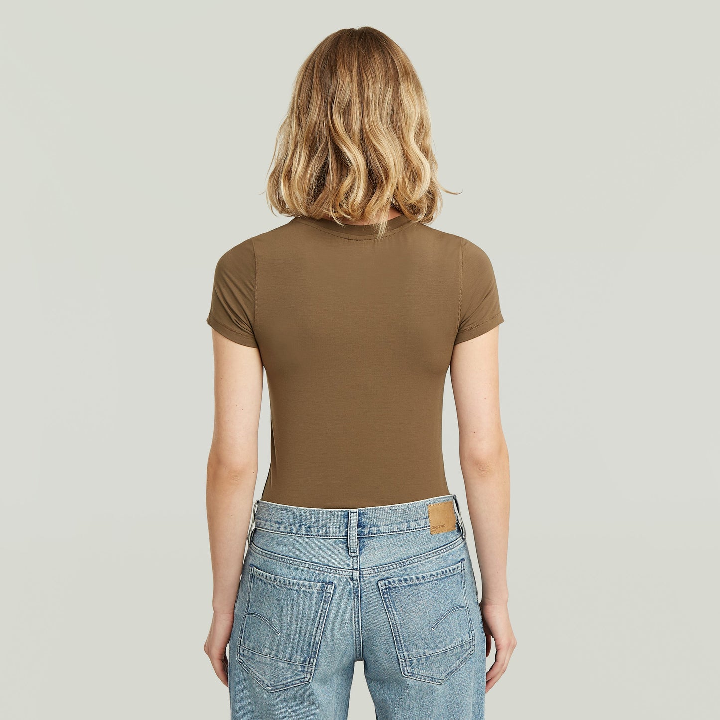 Mujer de espaldas usando una ajustada camiseta de modal marrón con diseño elegante y corte cómodo.