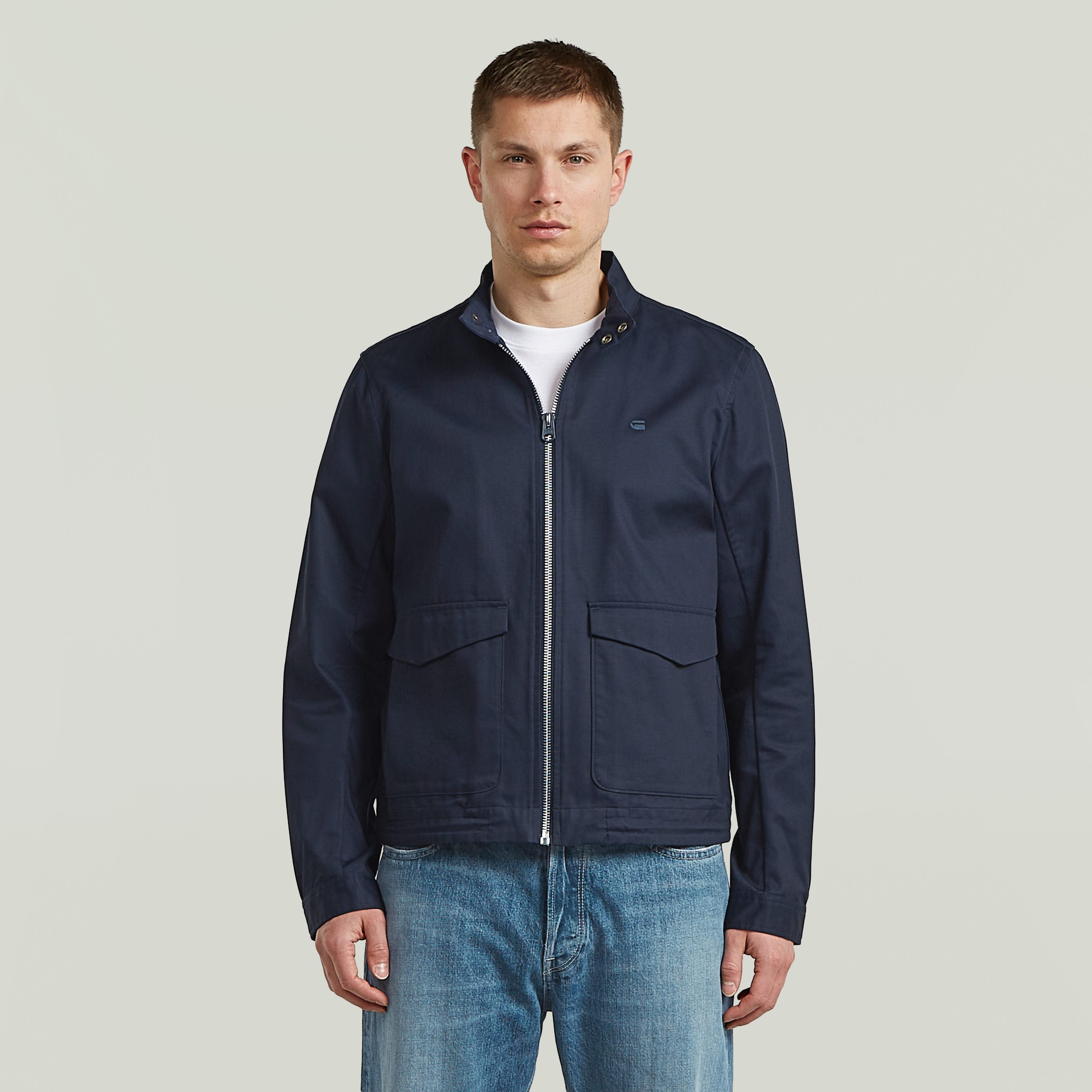 Hombre usando chaqueta ligera de algodón reciclado en azul oscuro, con cuello alzado y cierre de cremallera.