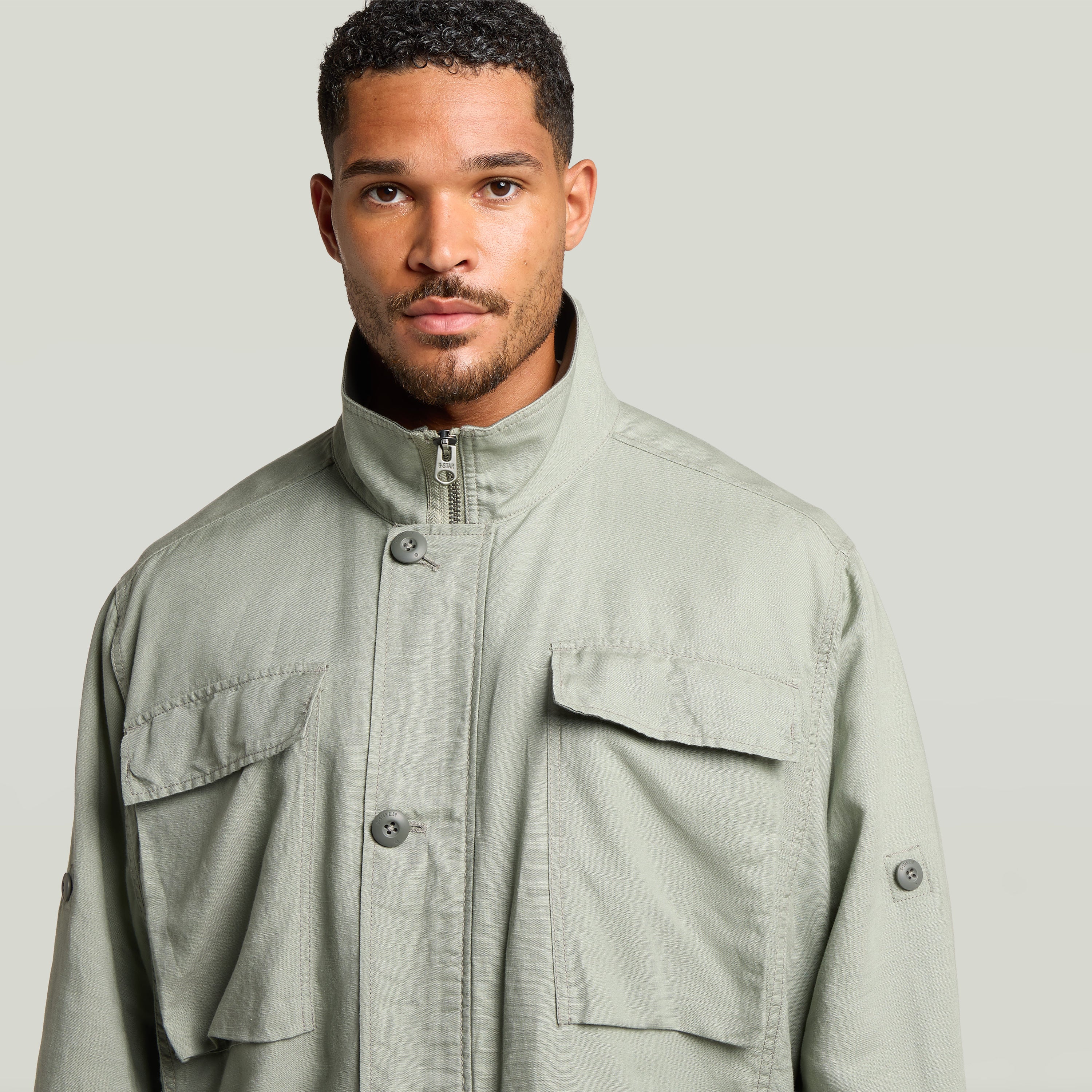 Close-up of a man wearing a versatile field smock jacket in light green with a raised collar and button closures.