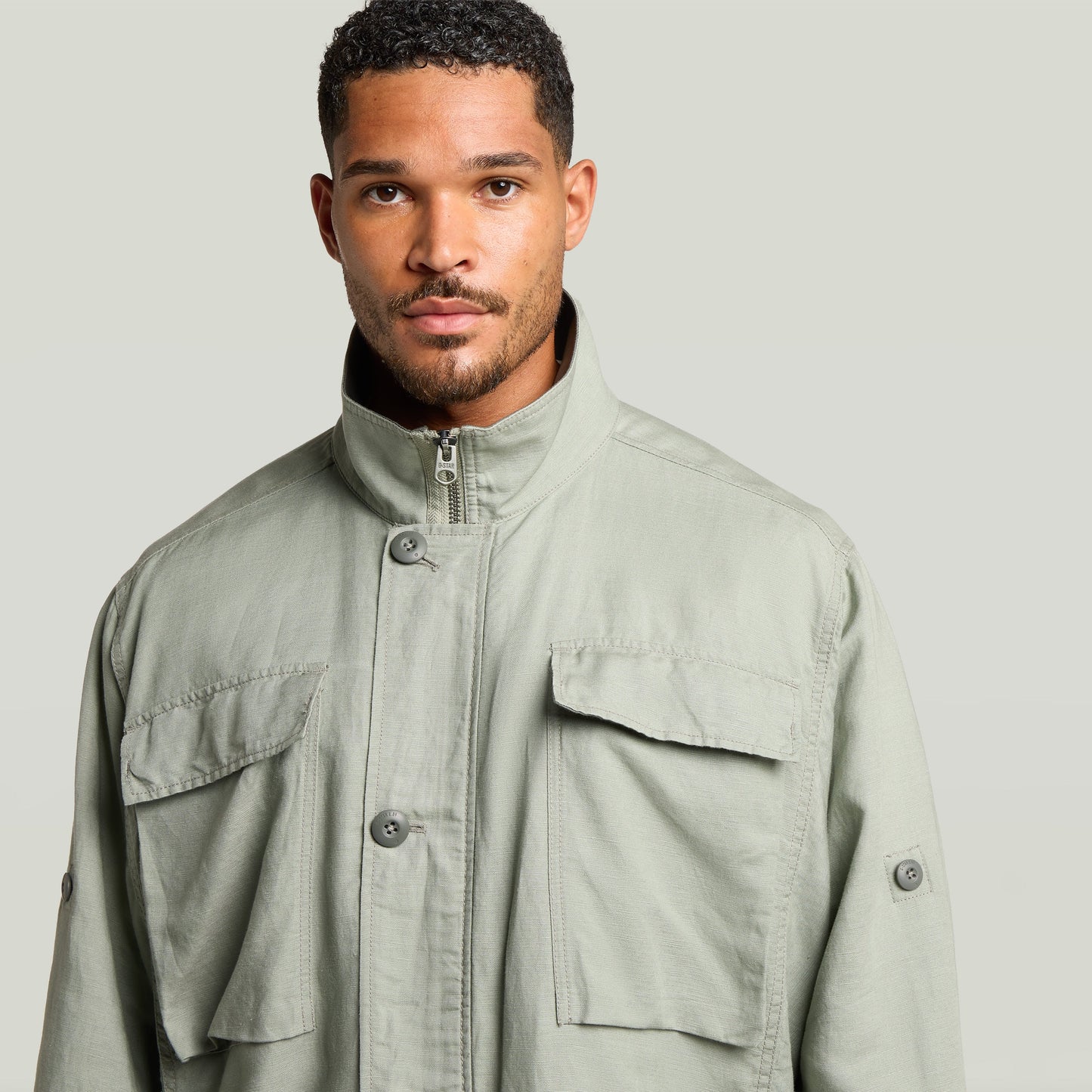 Close-up of a man wearing a versatile field smock jacket in light green with a raised collar and button closures.