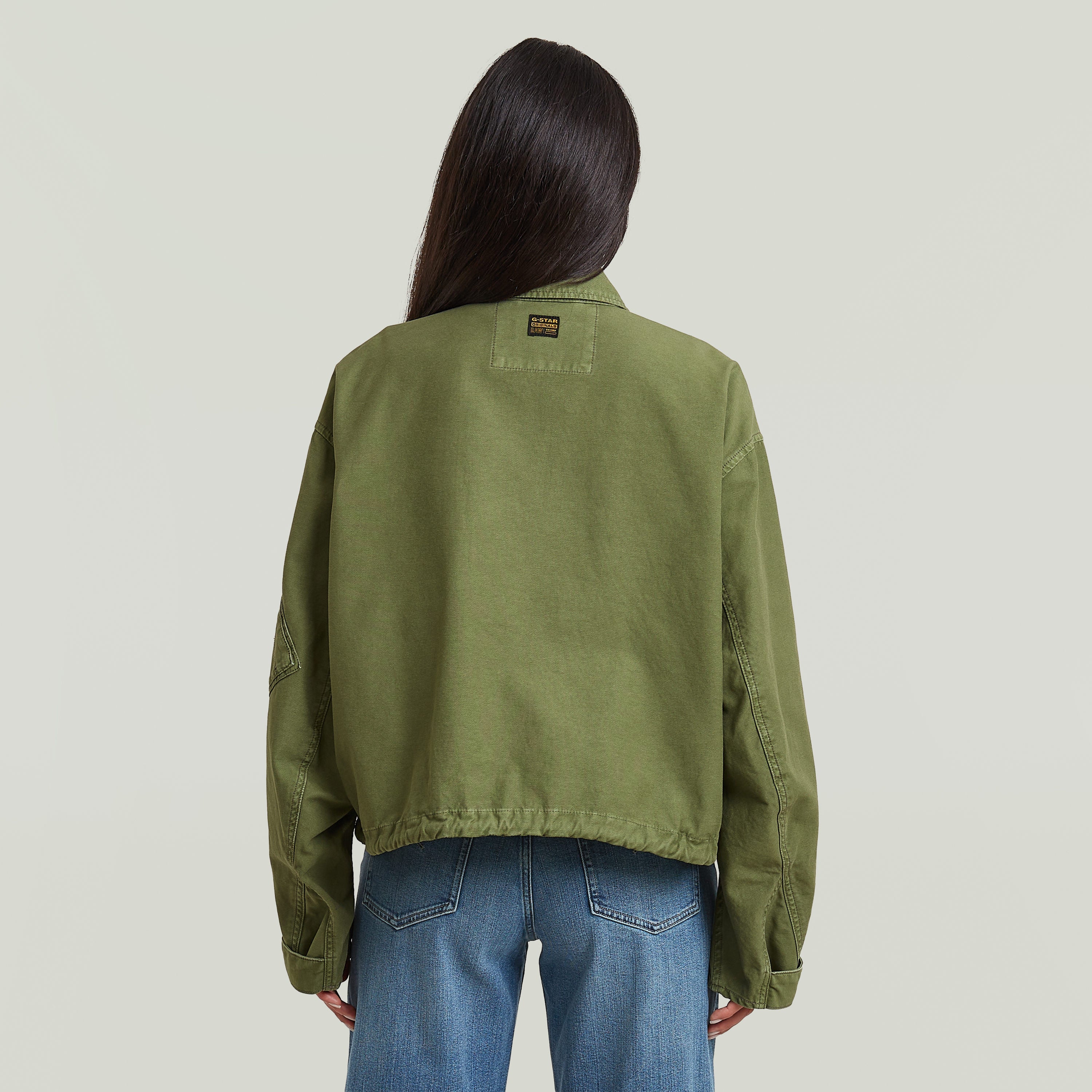 Mujer usando una chaqueta oversized cropped verde desde la parte trasera, mostrando el diseño relajado y el bajo elástico.